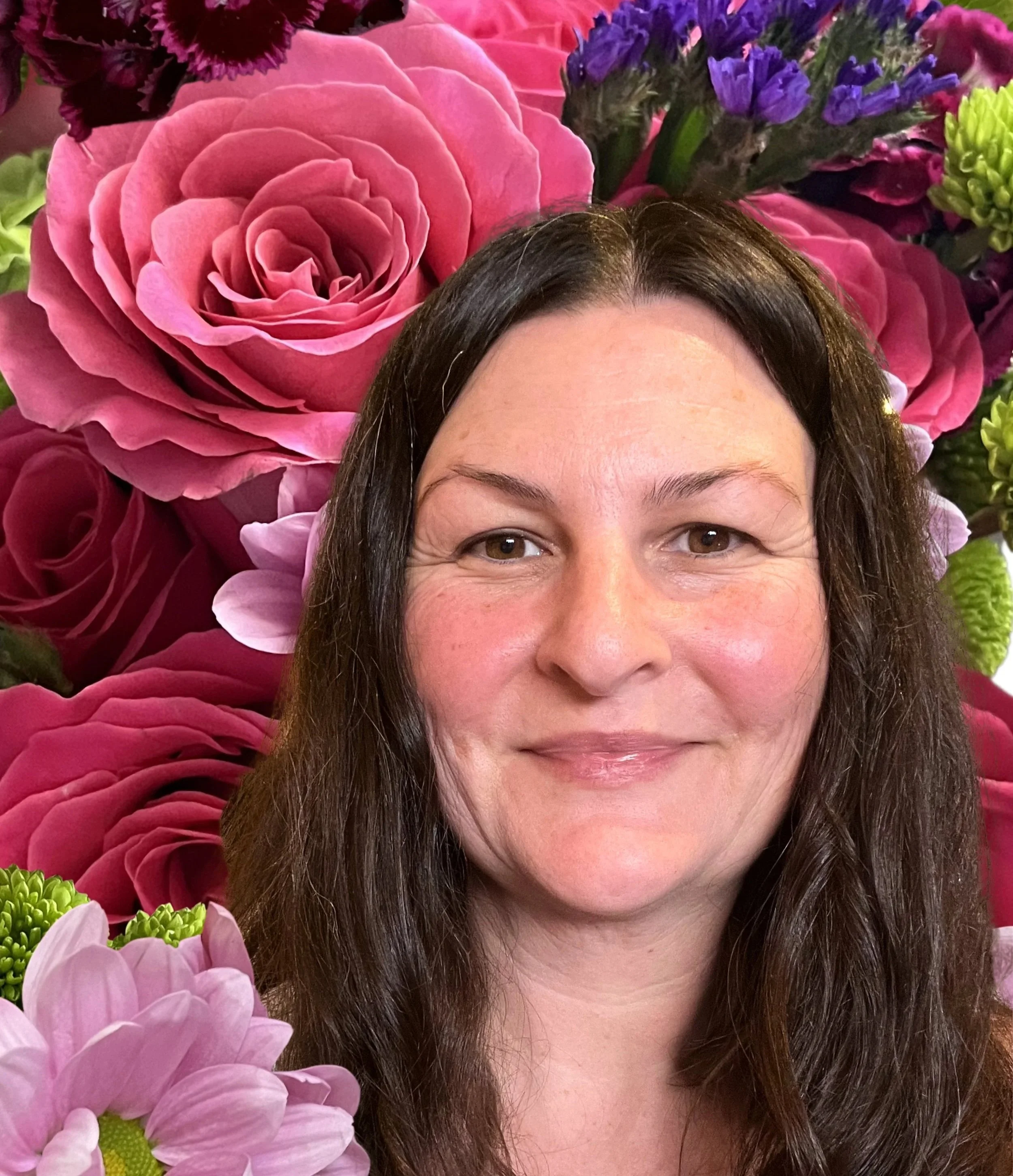 On a floral background, me! A smiling woman with light skin, dark hair, and rosy cheeks.
