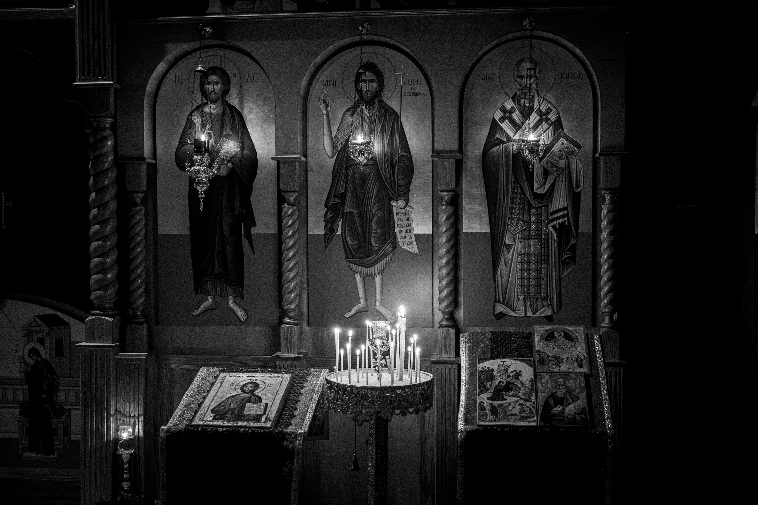 A black and white photo of religious icons in a church, depicting Jesus Christ and saints with candles in front.