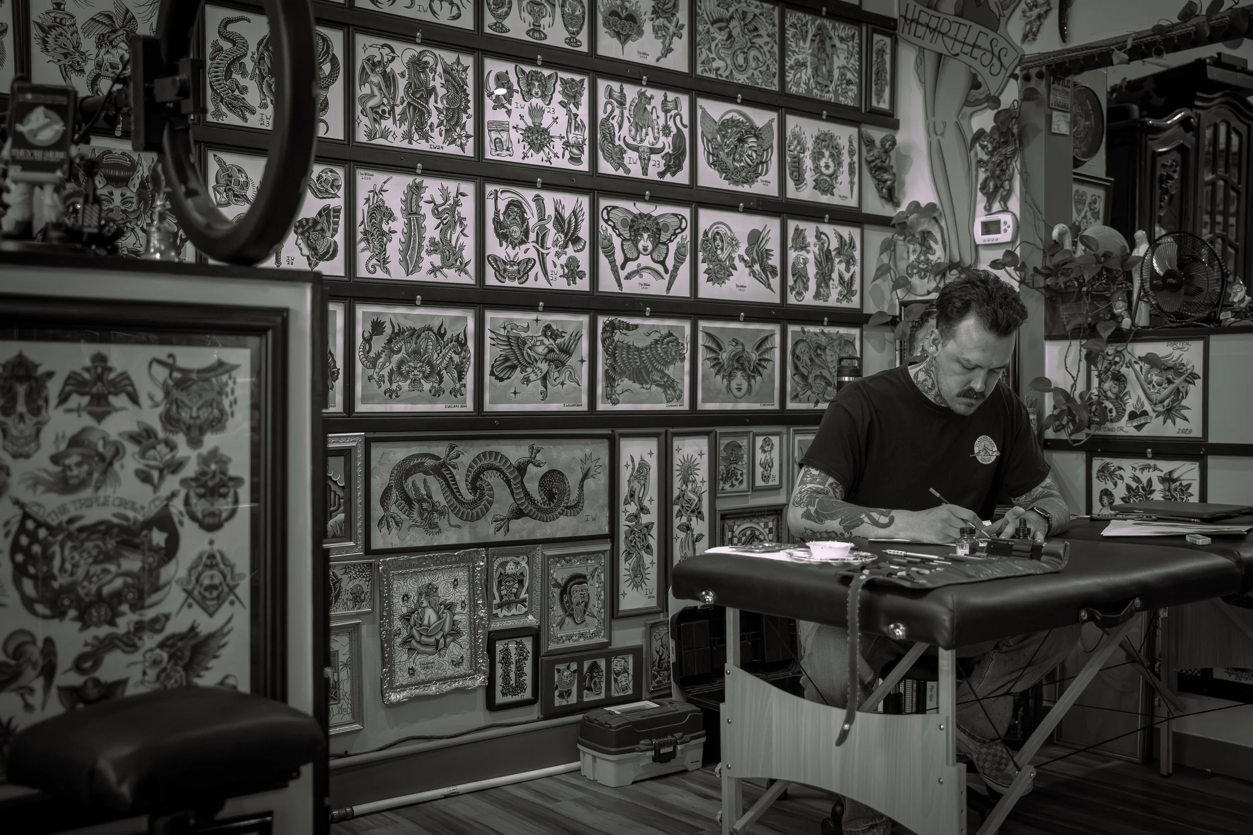 A tattoo artist working at his station, surrounded by framed tattoo artworks on the wall, in a tattoo studio.