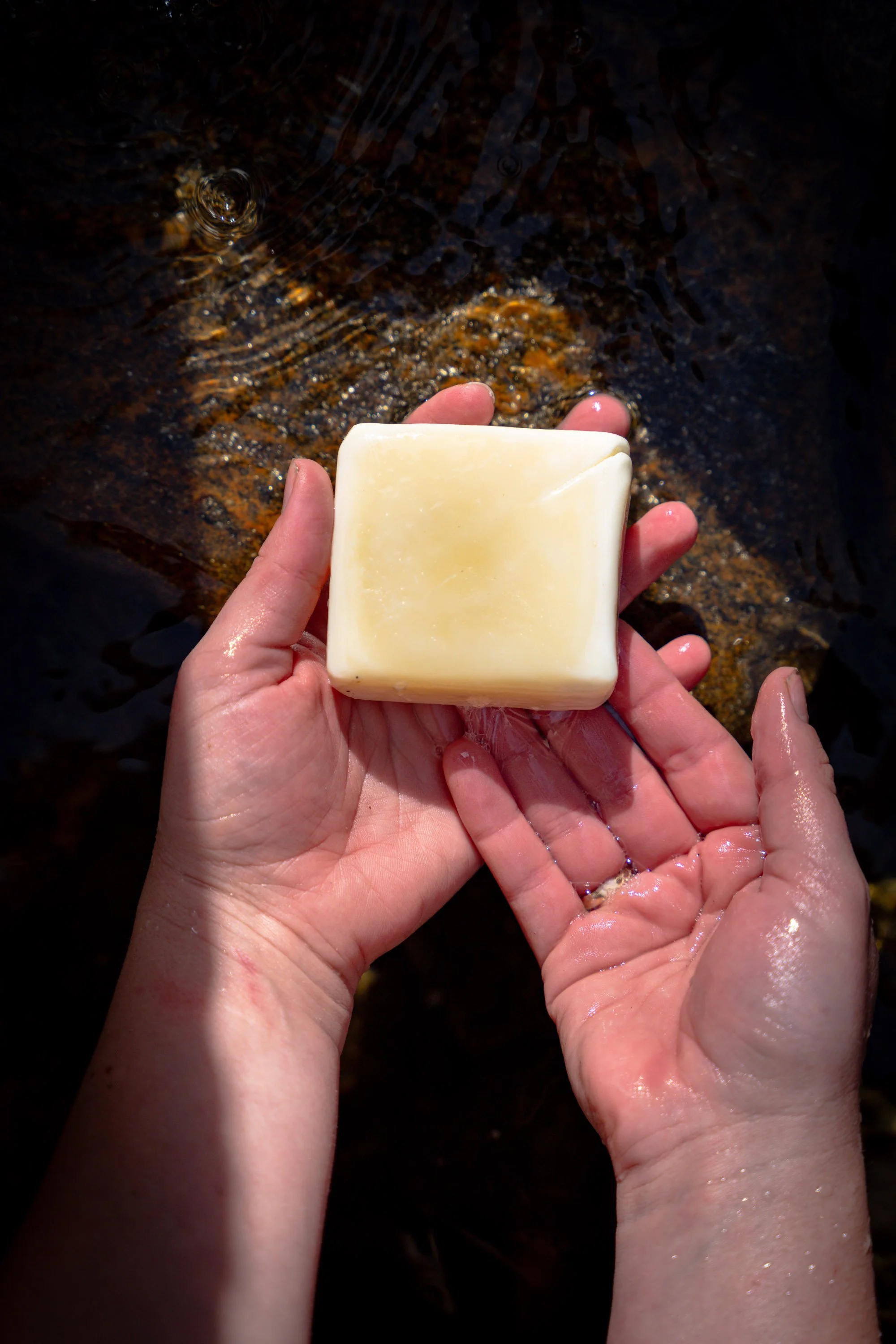 Person holding a bar of soap with water running over their hands in a stream of water.