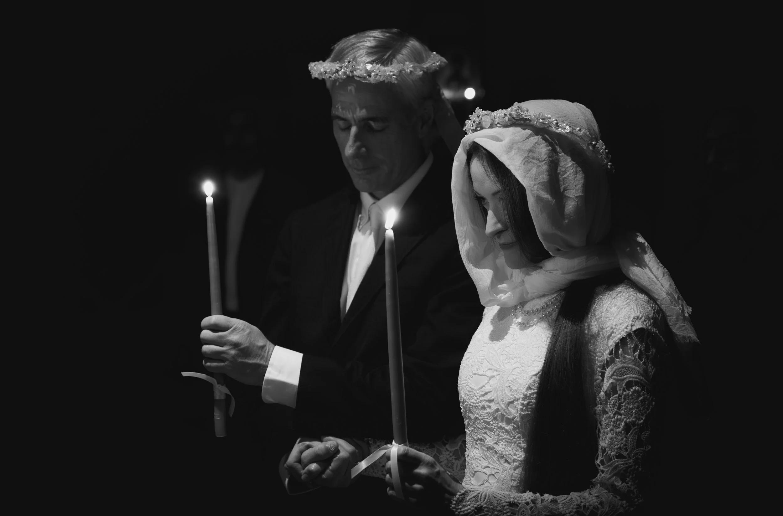 Black and white photo of a man and woman praying, holding candles, with their eyes closed and wearing crowns.