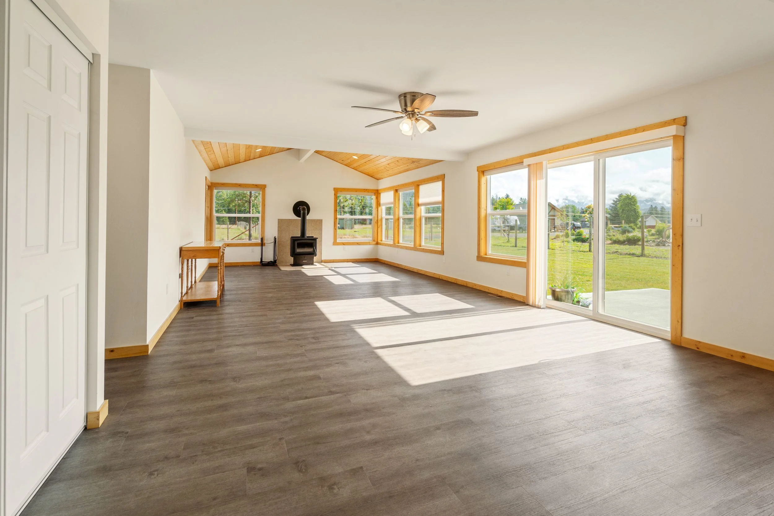 Living room with large windows, sliding glass door, ceiling fan, wood accents, and a view of a grassy yard outside.