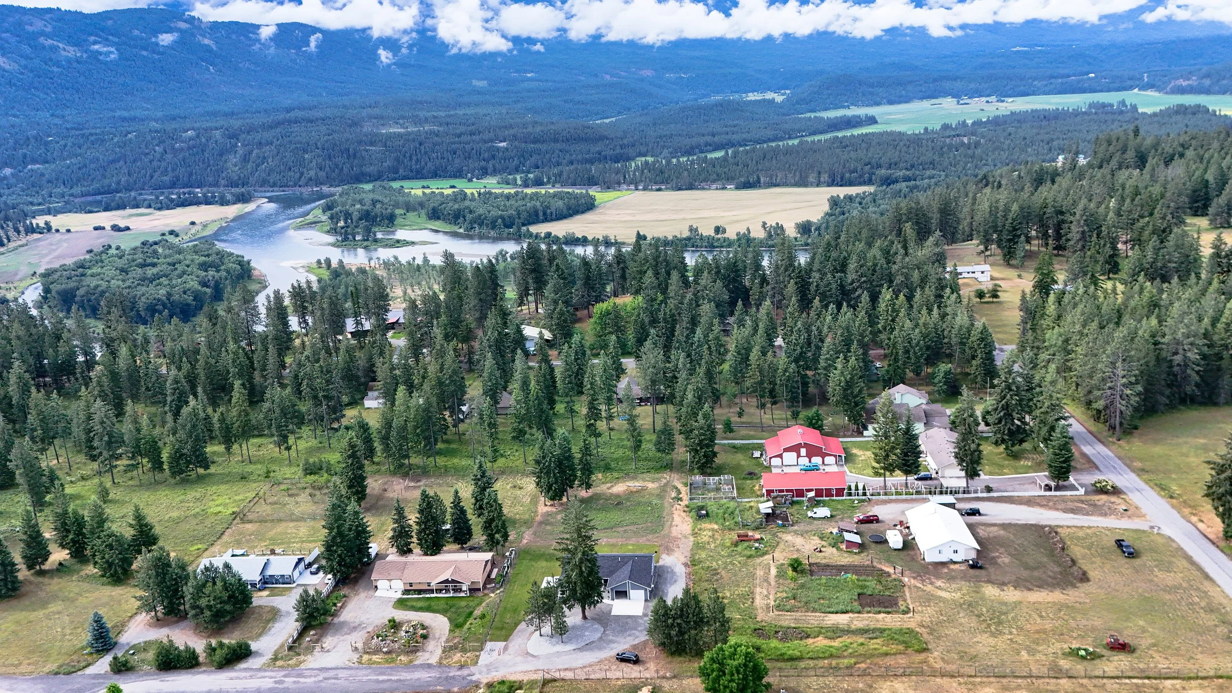 Aerial view of a rural landscape with houses, trees, fields, and a winding river amidst mountains and hills.
