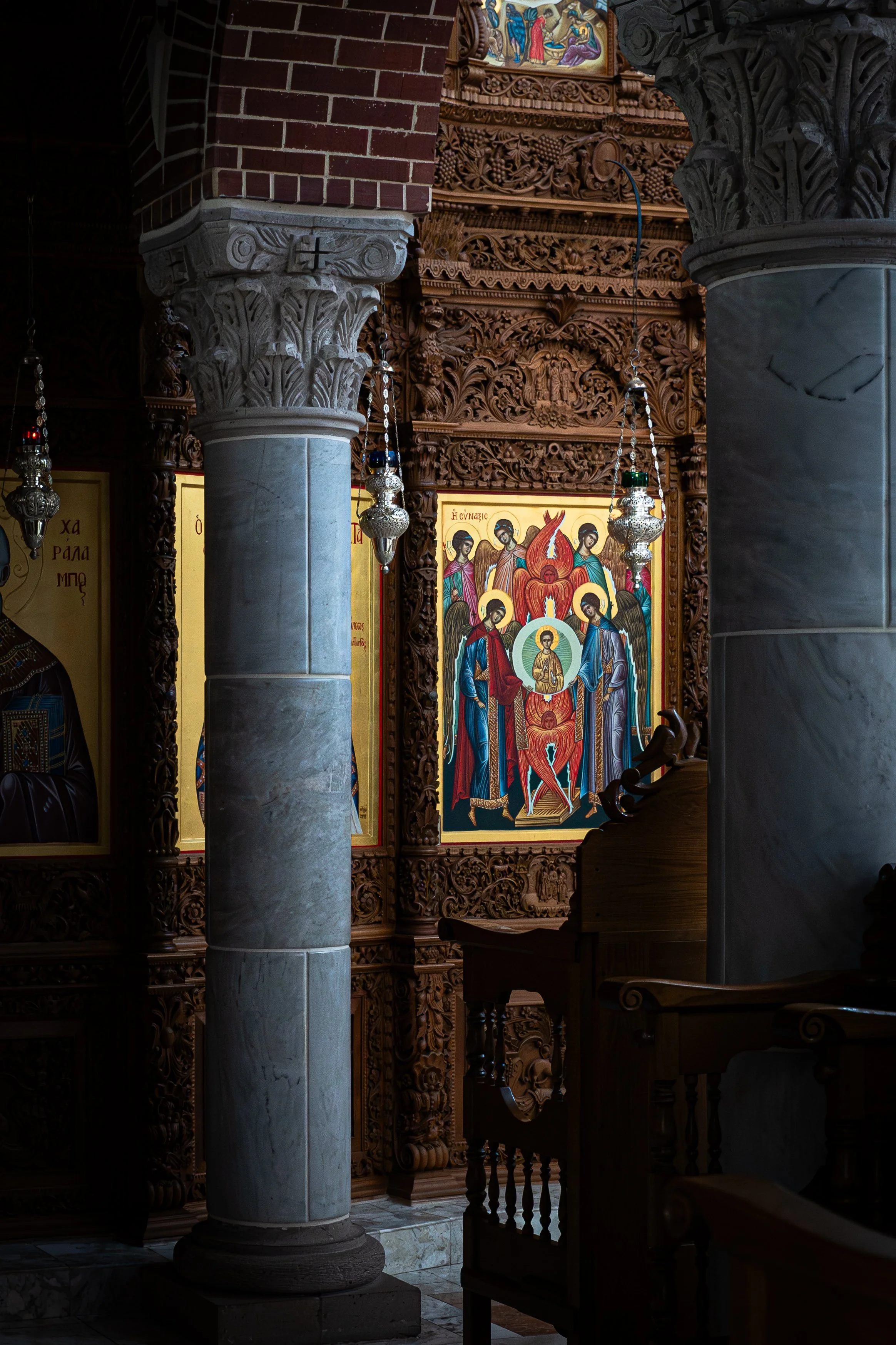 Interior of an ornate church with large marble columns, intricate wood carvings, religious icons, and hanging lamps.