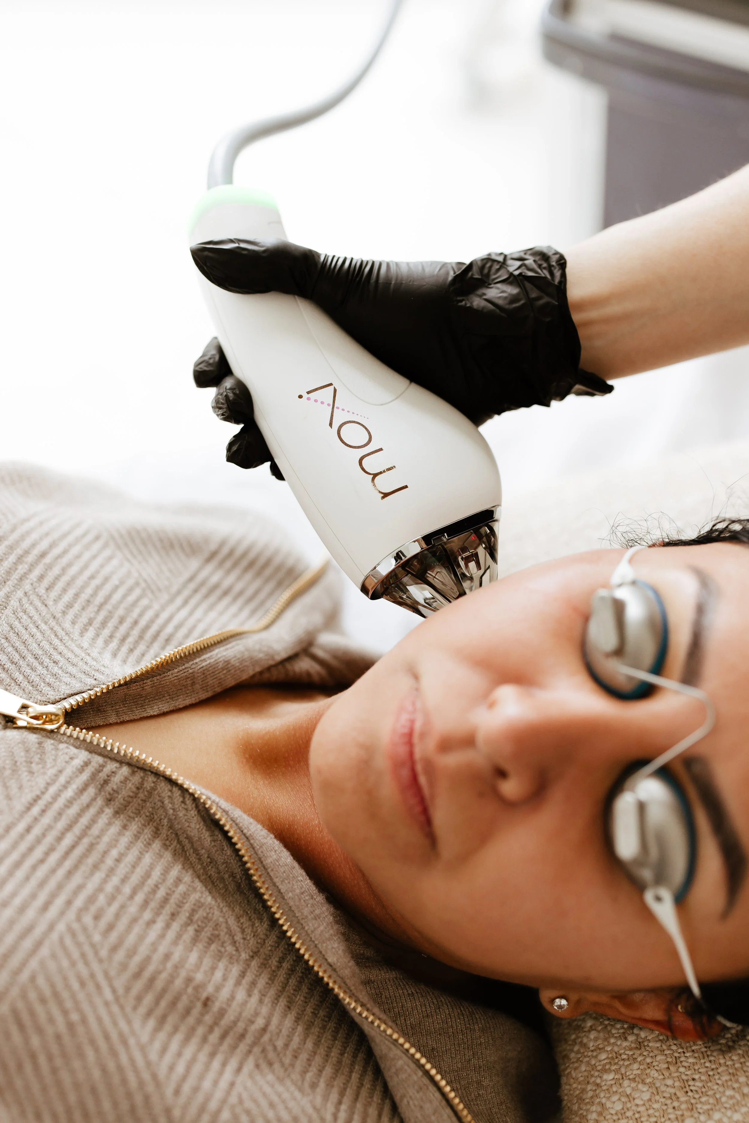 Person receiving laser or skin treatment wearing protective glasses, technician holding a device labeled 'Moxi'.