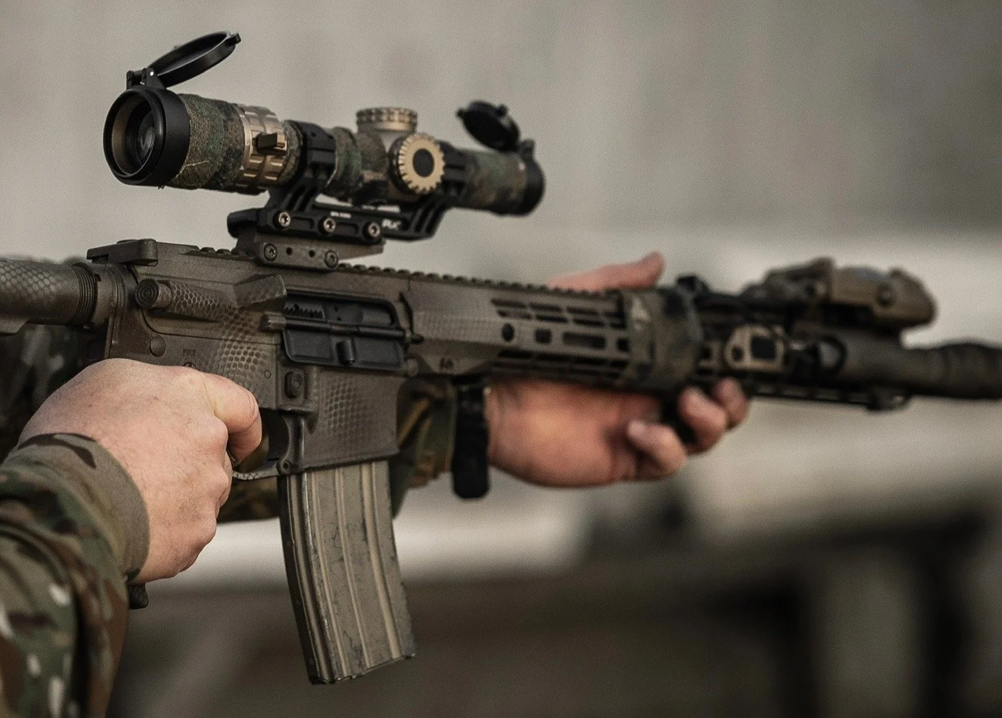 A person holding an AR15 with a mounted LPVO and PEQ-15.