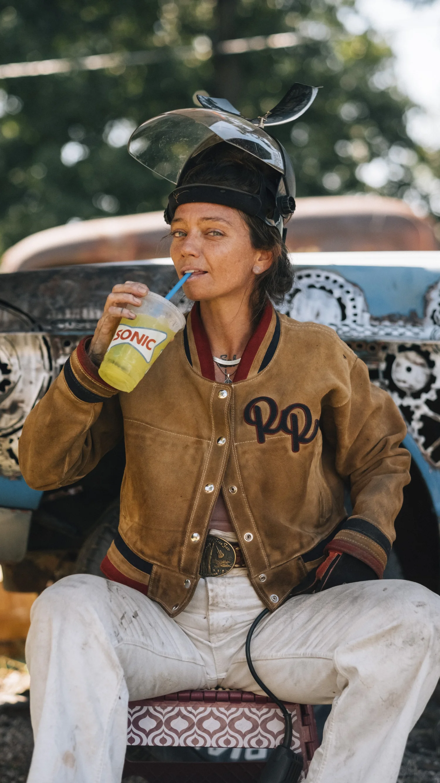 Rae Ripple in motorcycle gear beside a vintage car