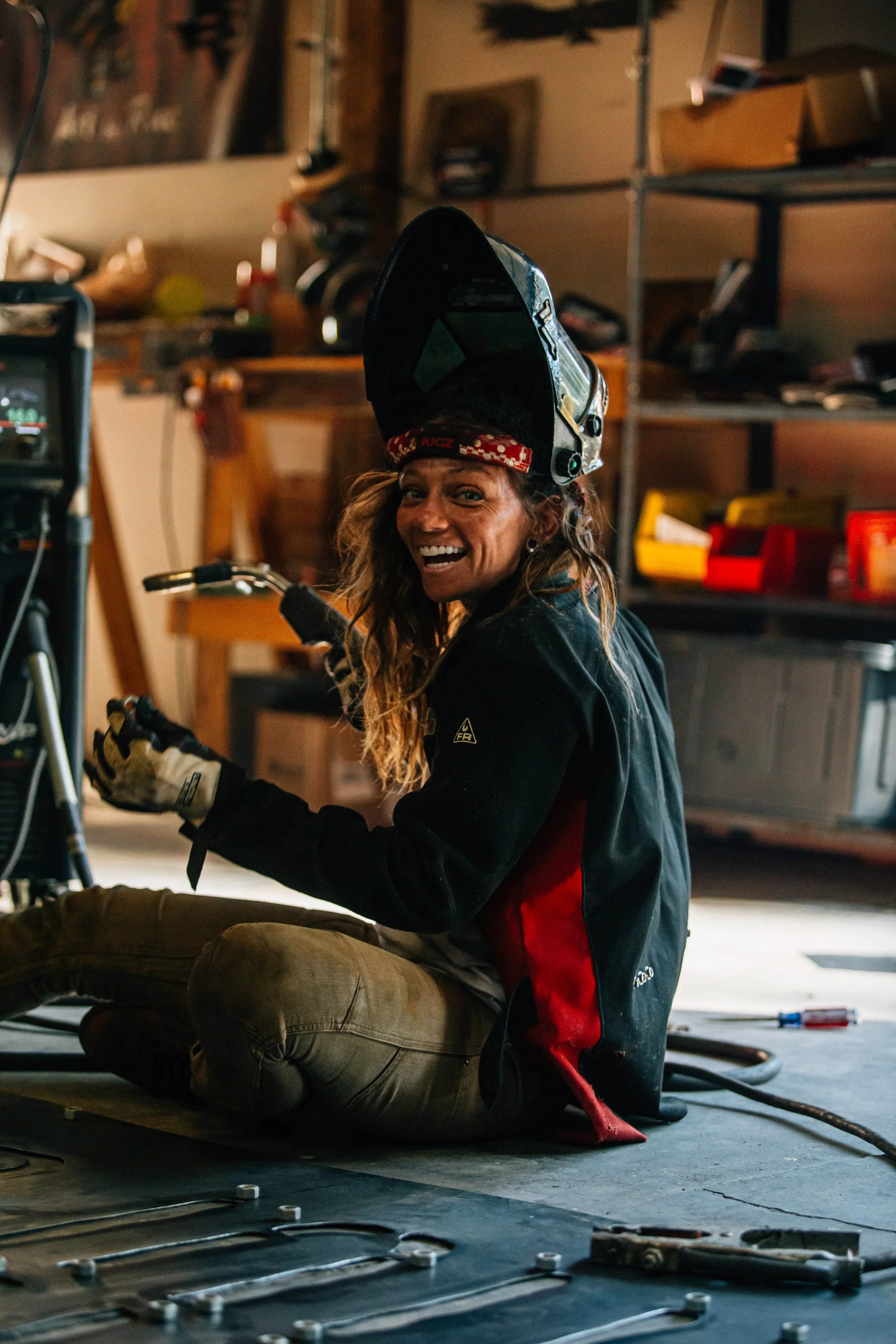 Rae Ripple smiling in her workshop with her welding helmet