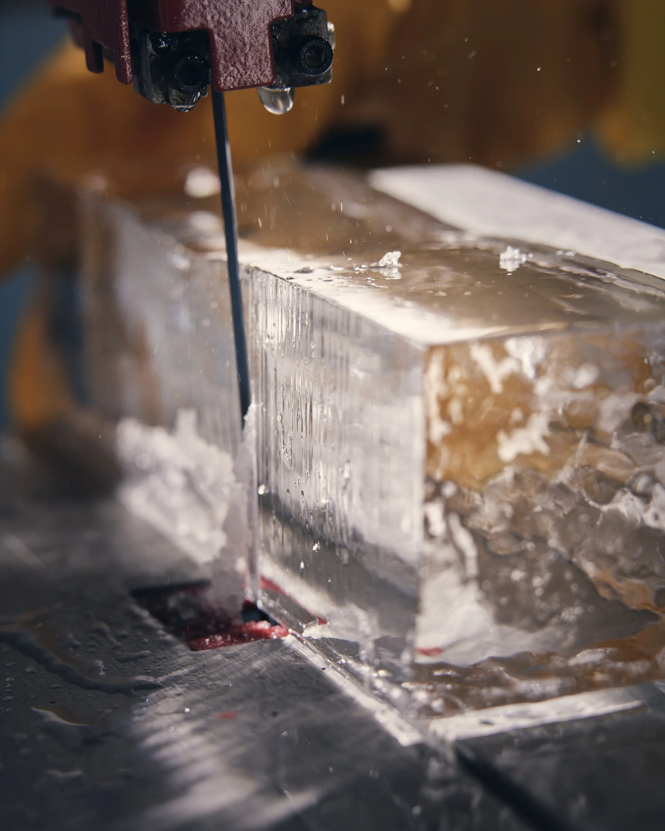 Close-up of a hacksaw cutting through a block of ice, with water and ice shavings splashing around.
