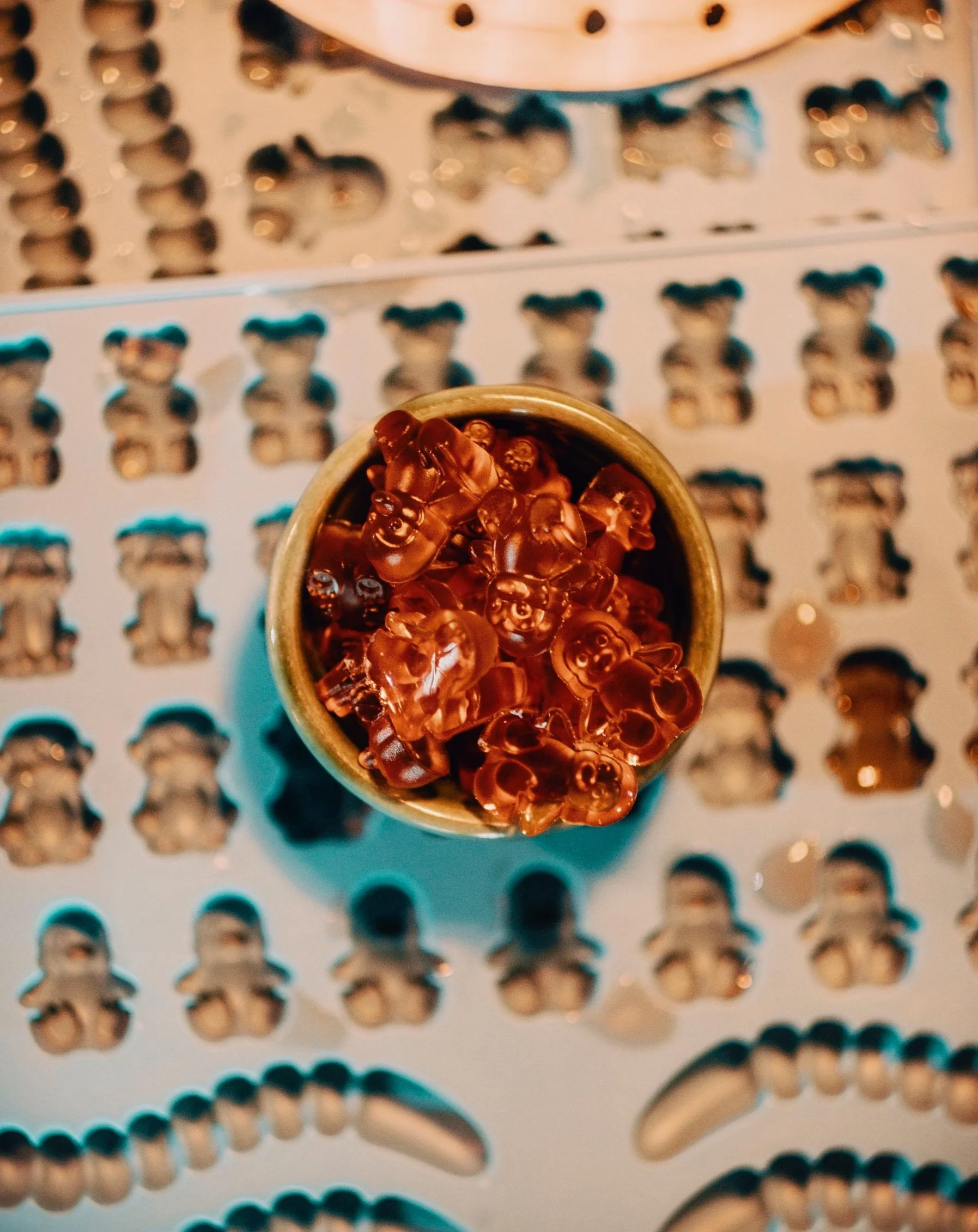 Top view of a small container filled with gummy bear candies, placed on a baking sheet with maze-like holes and shapes.