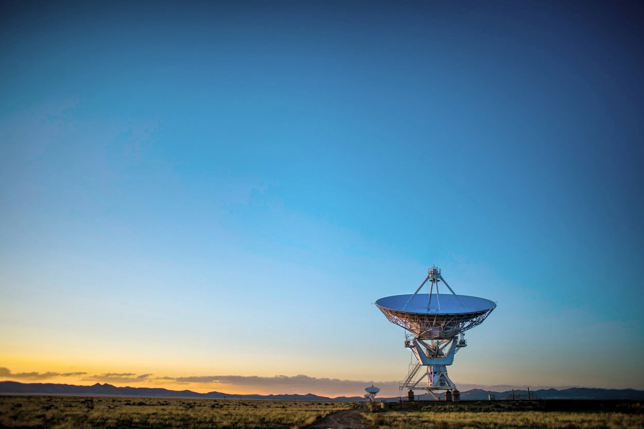 Satellite dish in desert landscape at sunset with clear sky.