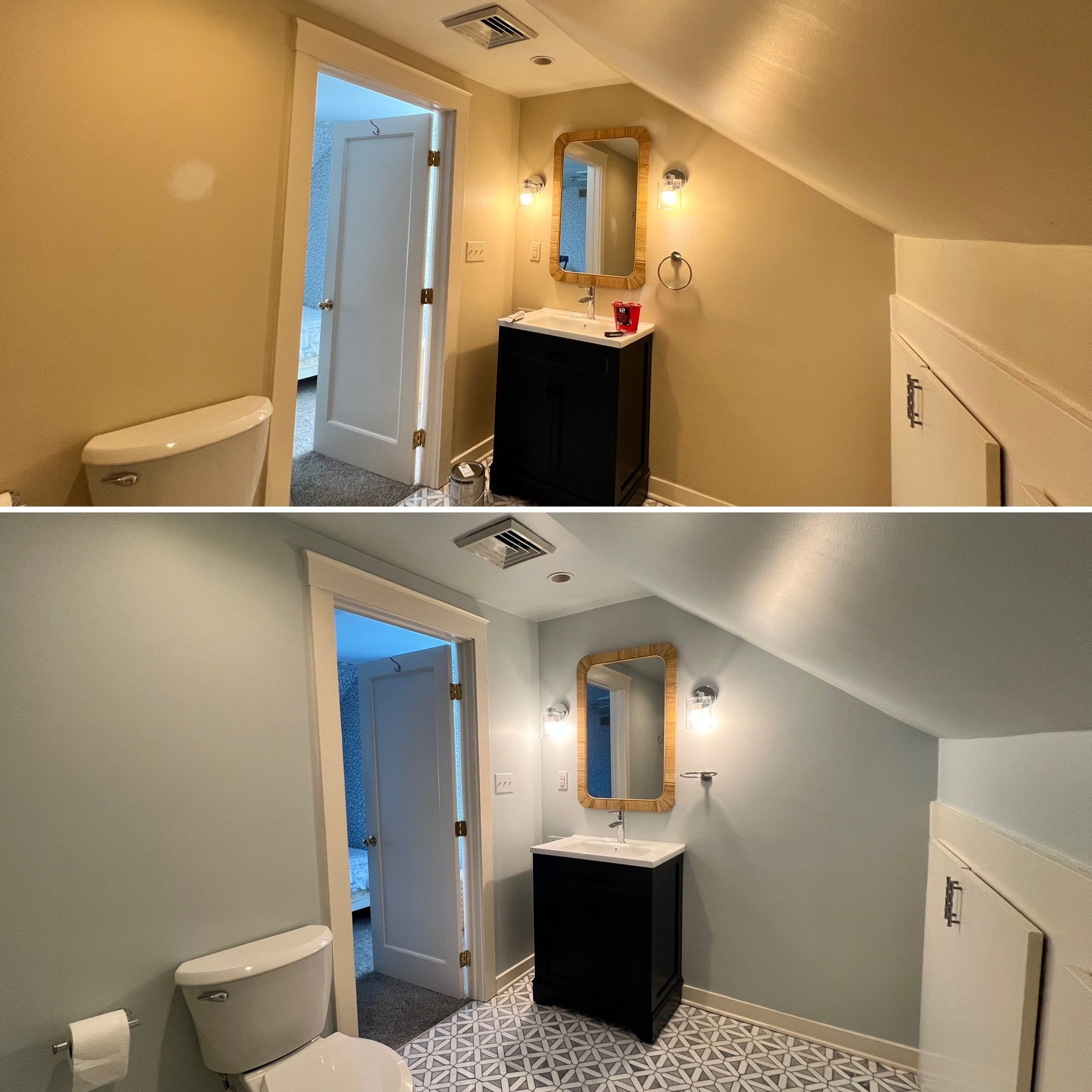 A bathroom with a white toilet, a black vanity with a white sink, a mirror with a wooden frame, two wall-mounted lights, a door leading to a bedroom, and patterned floor tiles.