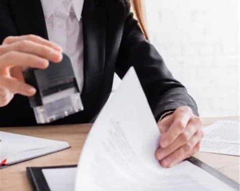 Person in business attire stamping documents on a desk.