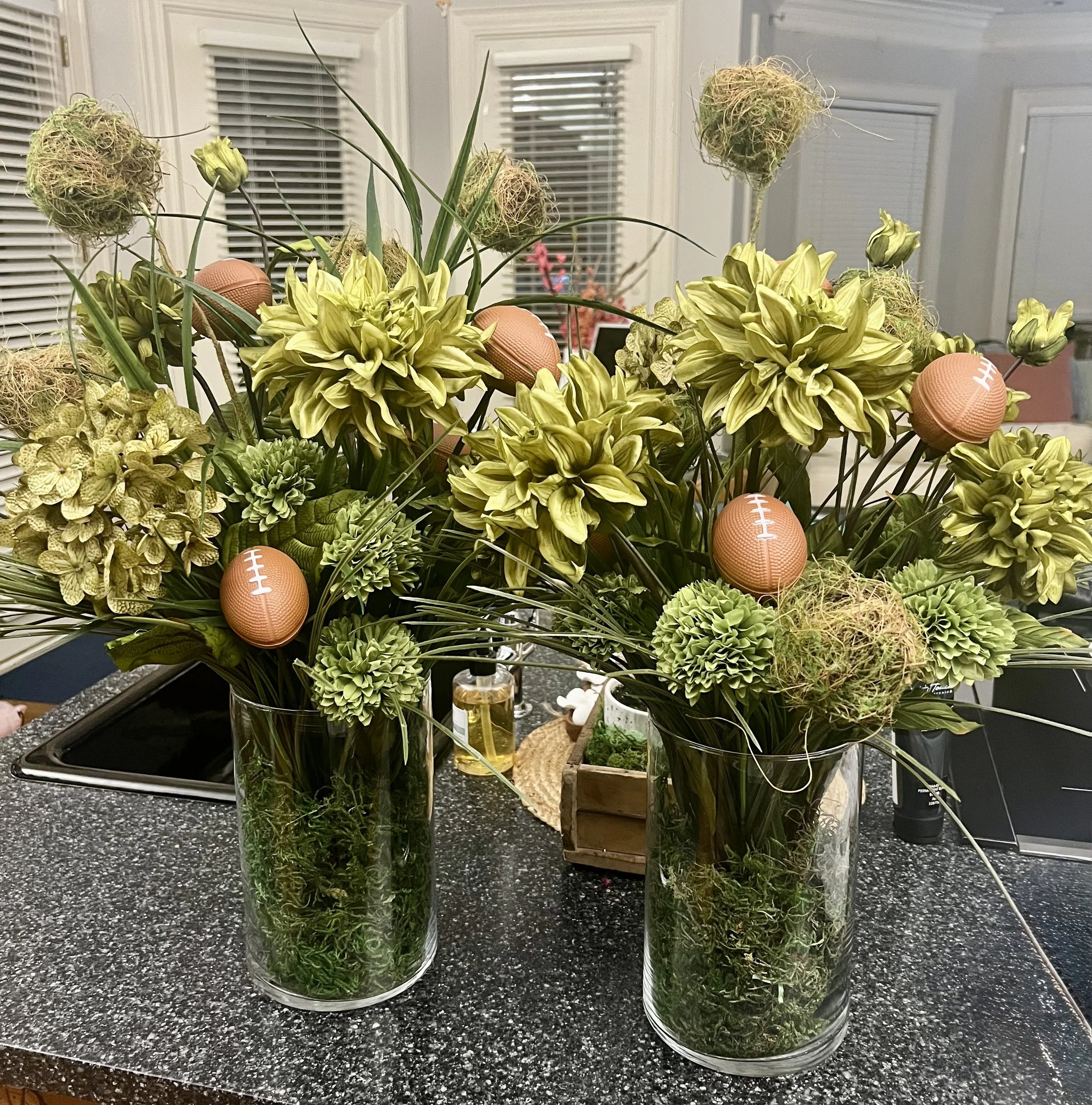 DIY football floral centerpiece in progress with greenery and footballs.