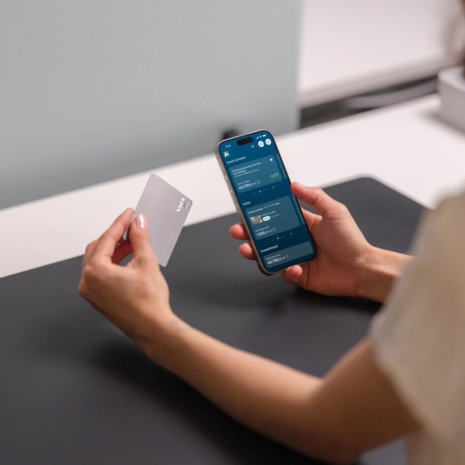 Person holding a smartphone displaying a mobile banking app and a credit card.