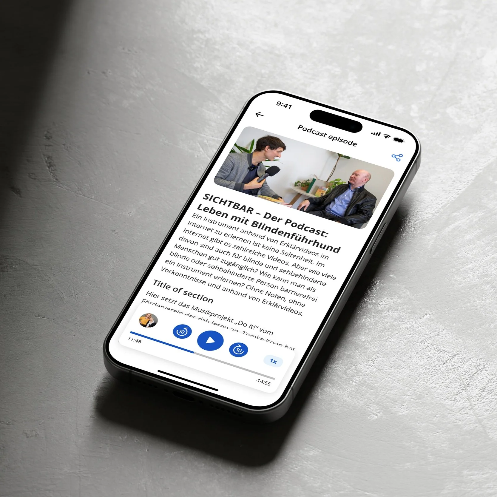 A smartphone displaying a podcast episode screen titled "SICHTBAR - Der Podcast" with an image of two people having a conversation. The podcast discusses life with a guide dog. The screen shows a play button and progress bar on a gray surface.