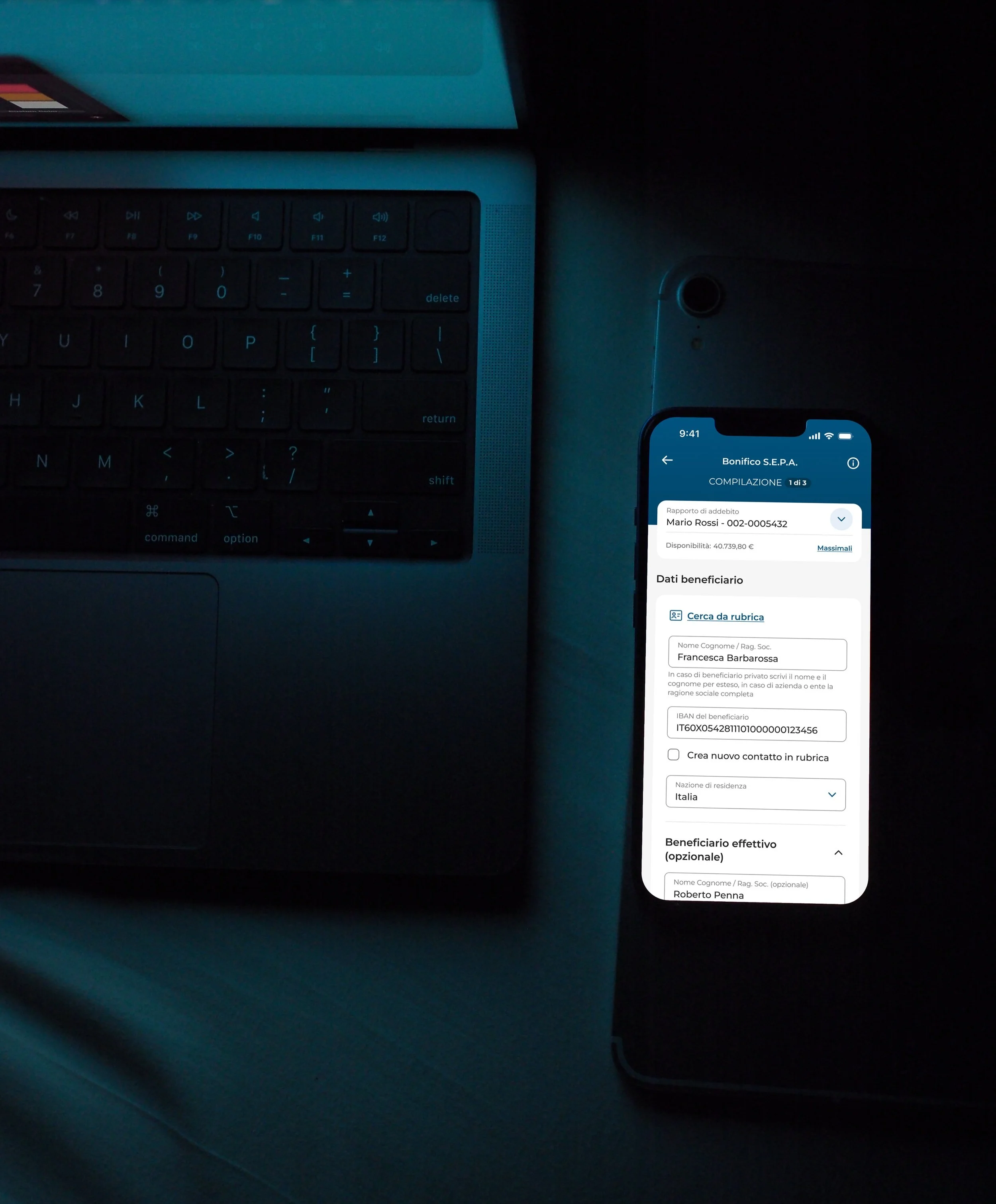 Dimly lit scene with a laptop keyboard and a smartphone displaying a banking app interface.
