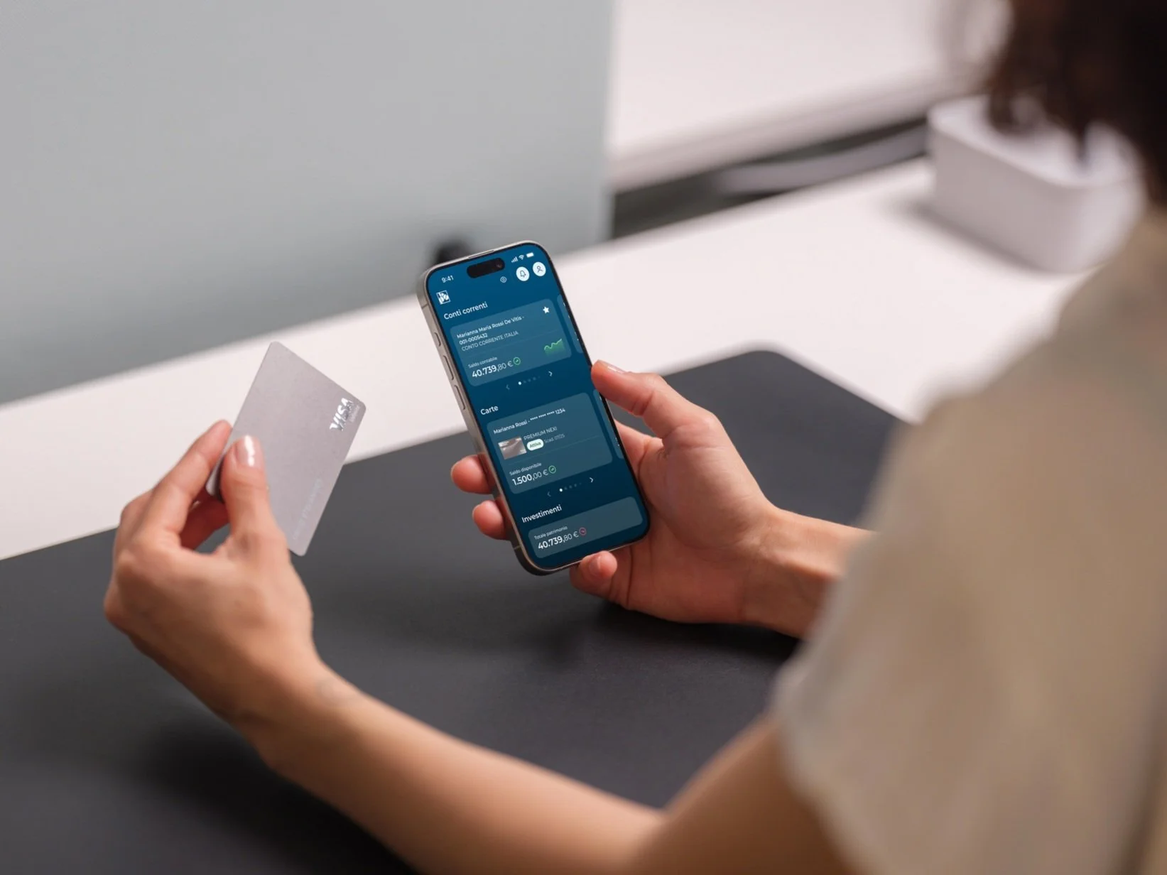 Person holding a smartphone displaying a banking app with balance information, and a debit card in the other hand.