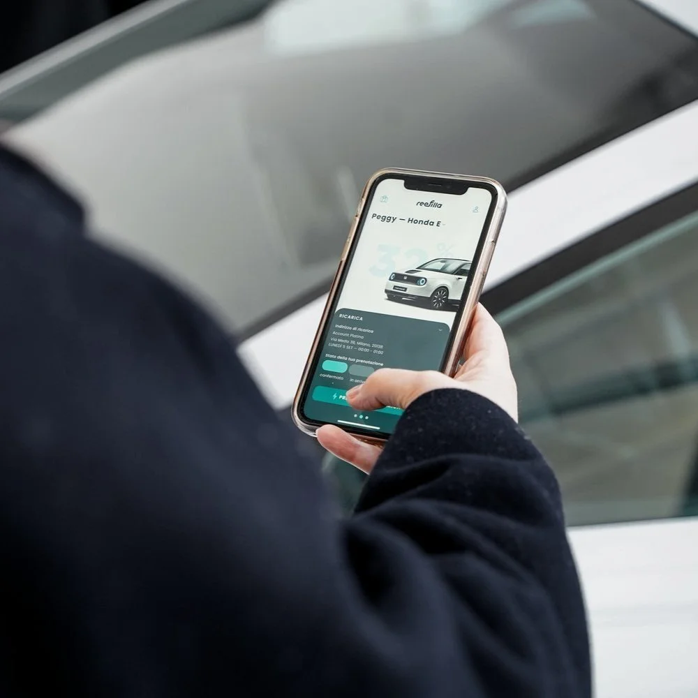 Person using a smartphone app to monitor electric car charging status next to a vehicle.