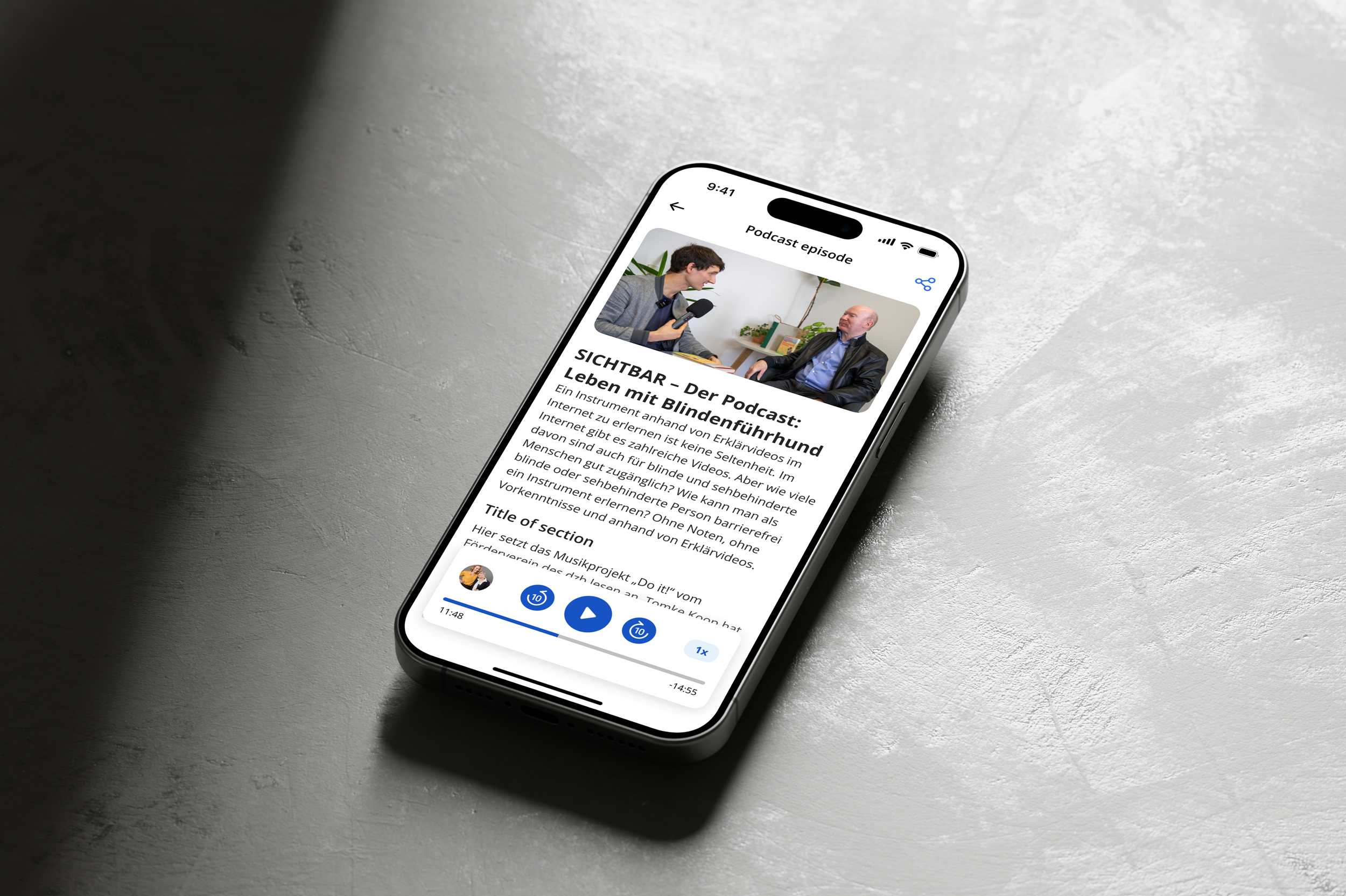 Smartphone on a gray surface displaying a podcast episode page with an image of two people conversing.