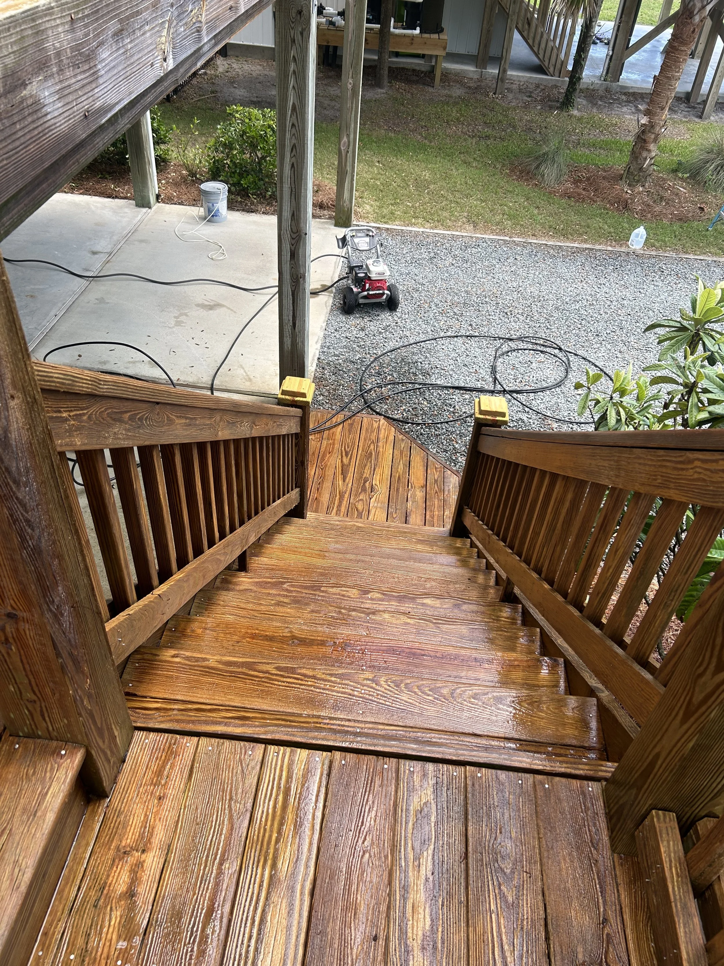 Wooden staircase leading down to a yard with a gravel area, a concrete patio, and some gardening supplies.