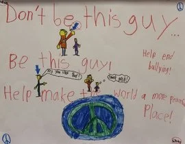 Child's drawing with messages for anti-bullying, including a peace symbol, people, and a rainbow, with phrases like 'Don't be this guy,' 'Be this guy,' and 'Help make a world a more peaceful place!'