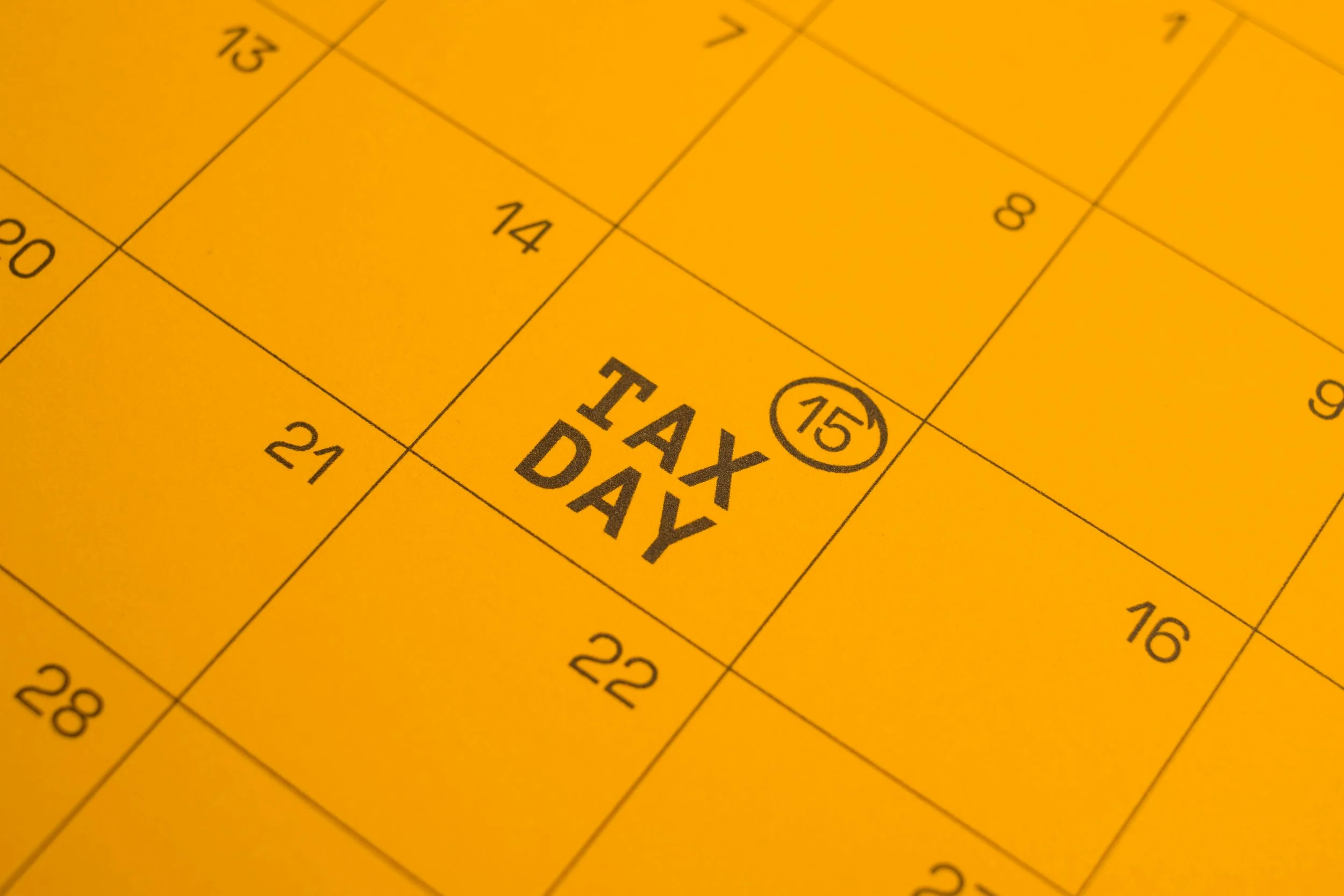 Close-up of a yellow paper Calendar with dates, showing the words 'Tax Day' and the number 15 in a circle.