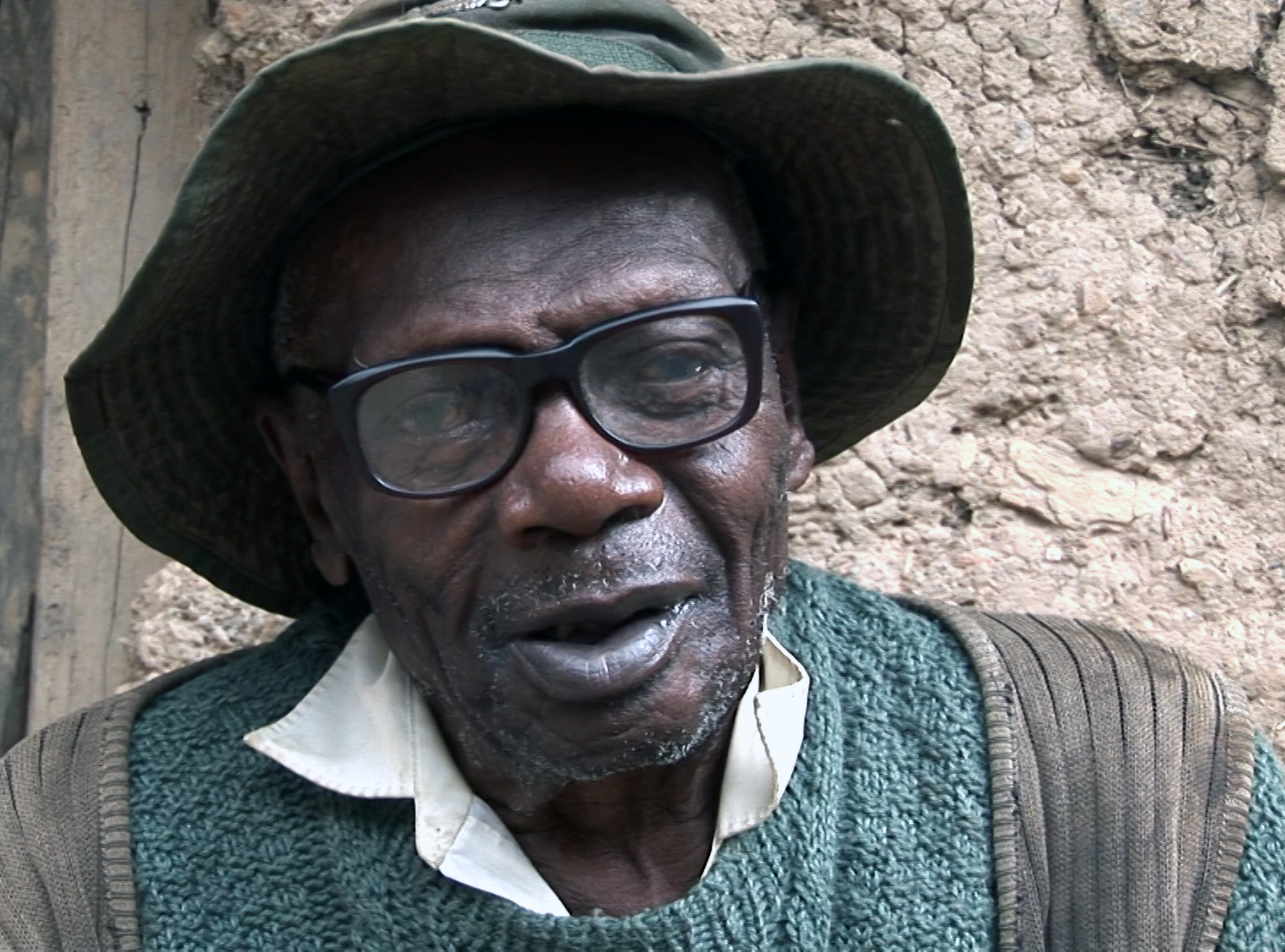 An elderly Afro-Bolivian man in glasses and a hat stares at the camera