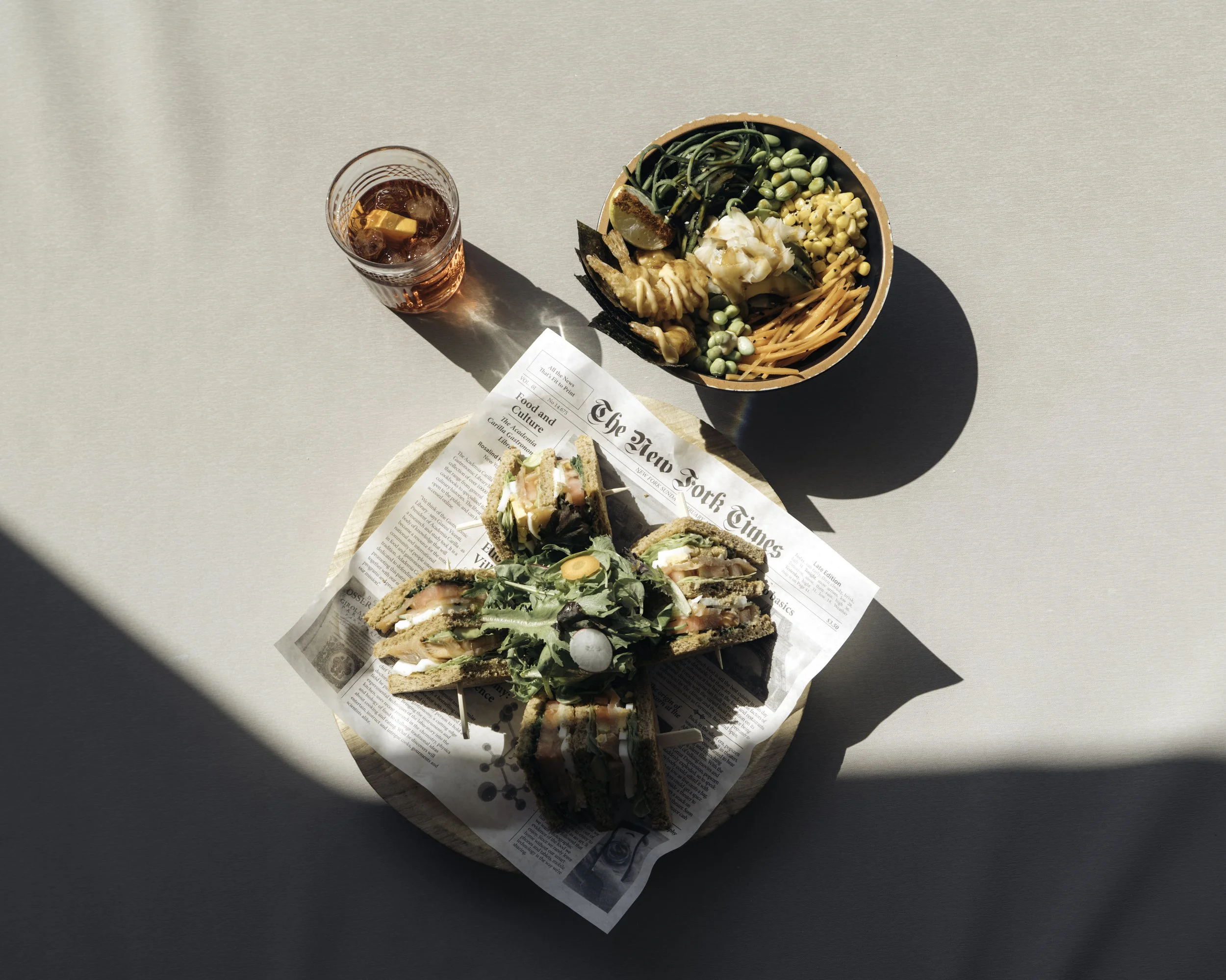 A meal of sushi sandwiches, a salad, and iced beverage on a light-colored table.