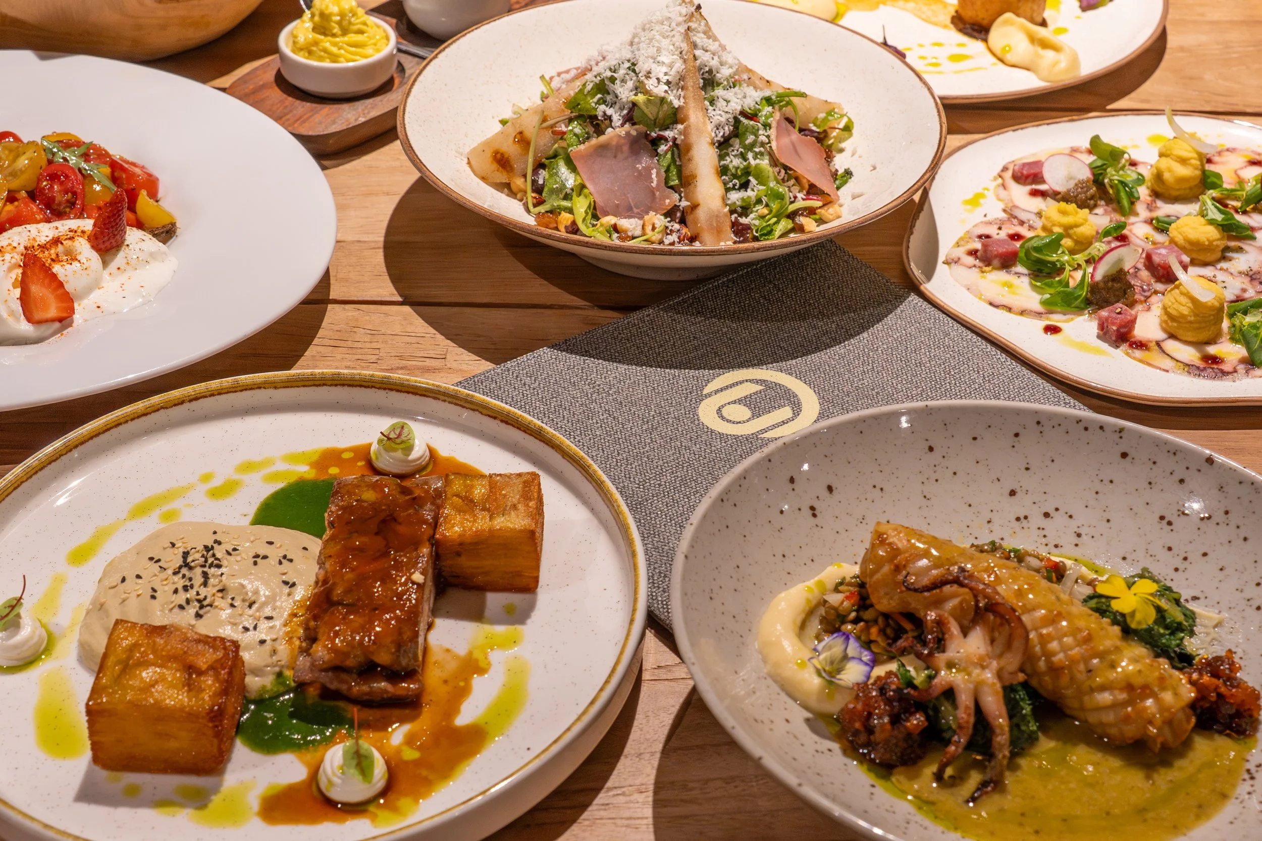 Assorted dishes of elegant cuisine featuring salads, roasted meat, seafood, and vegetables on a wooden table.