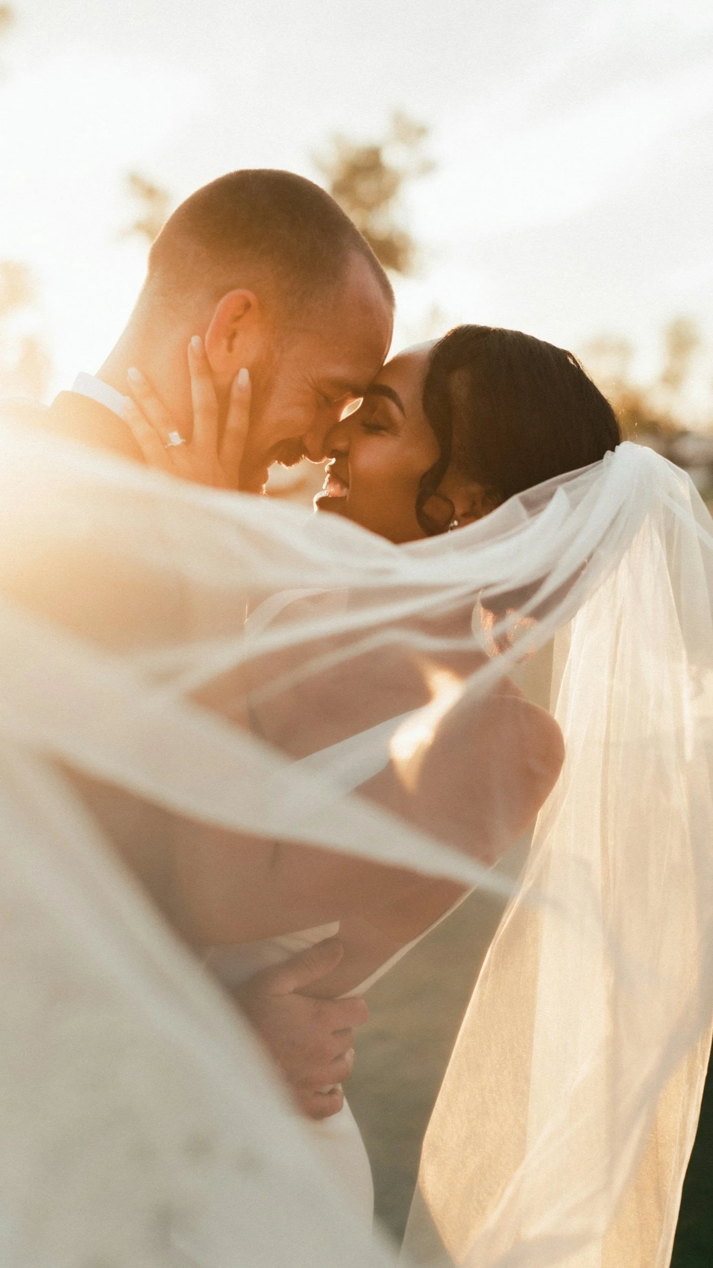 Bride and groom embracing under veil in soft sunlight.
