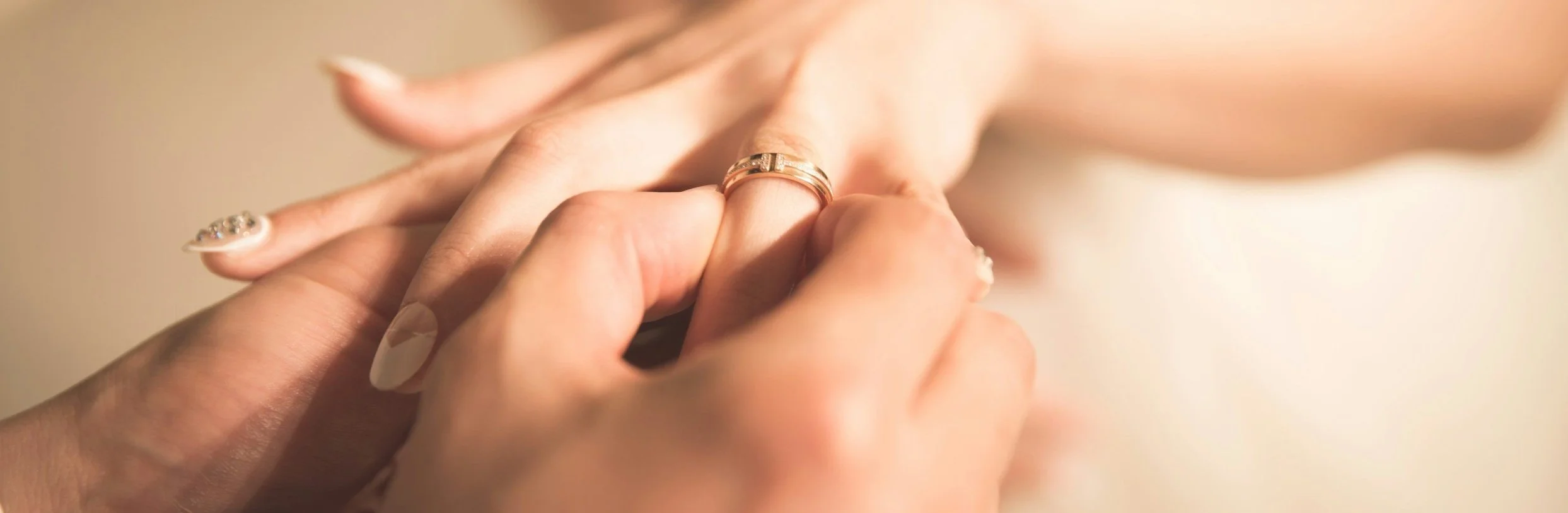 Close-up of a person placing a wedding ring on another person's hand.