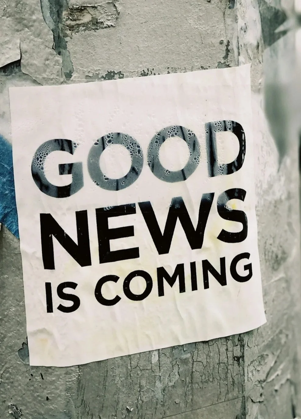 A sign sheet on a brick wall that reads, "GOOD NEWS IS COMING" with the letters in black, some filled with bubbles.