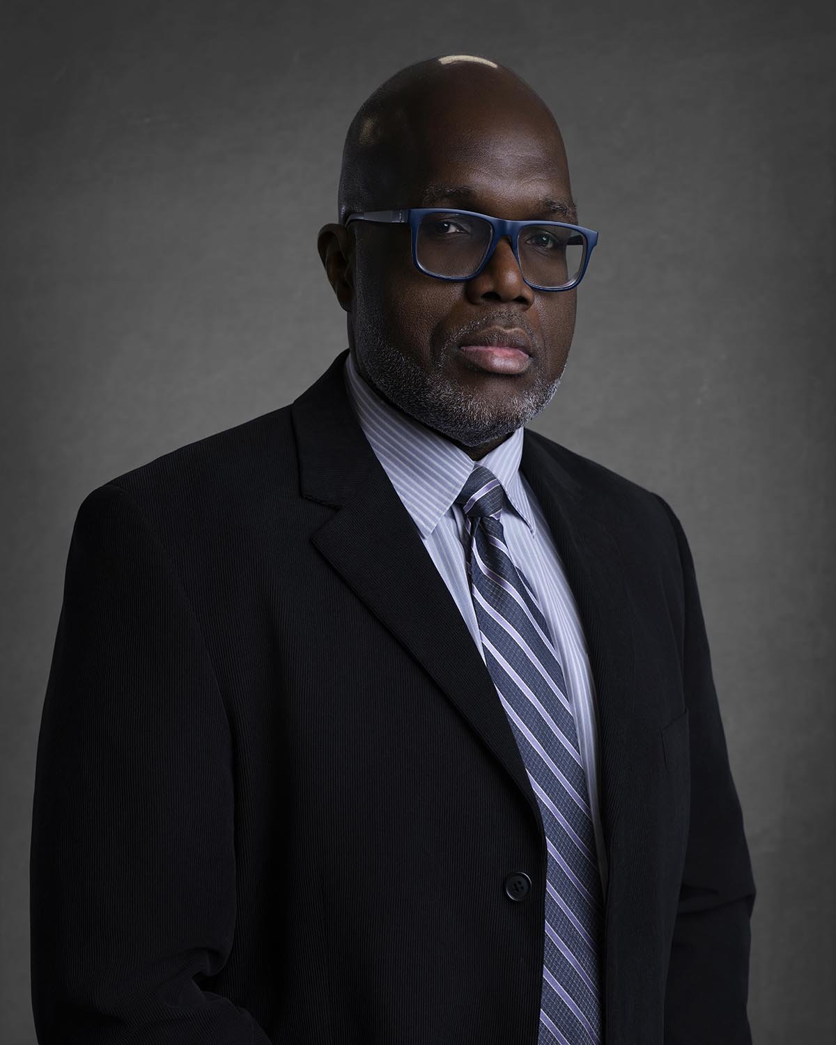 Person in a suit and sunglasses outdoors with trees in the background.