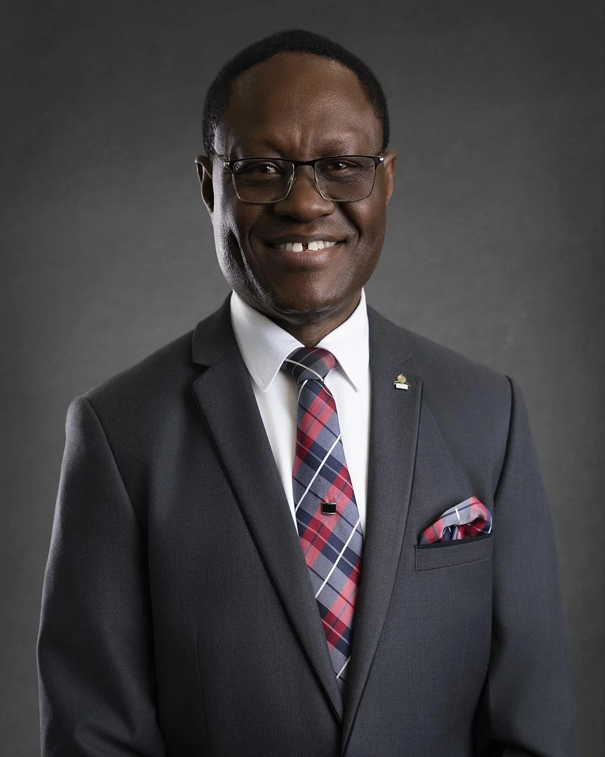 Man in a dark pinstripe suit with colorful tie and pocket square, wearing glasses, smiling against a neutral background.