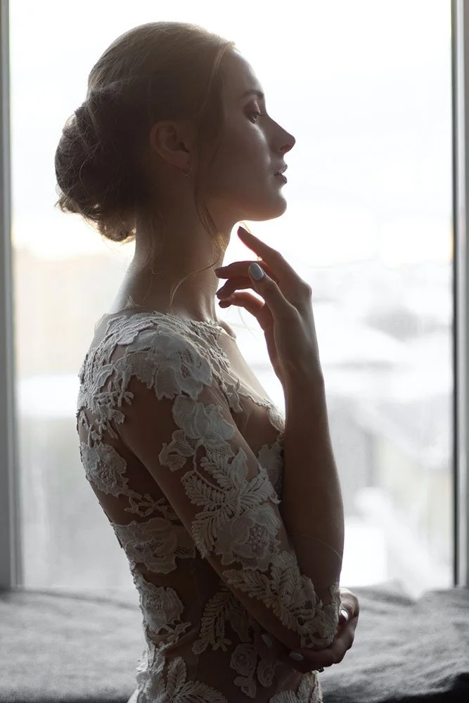 Silhouette of a woman in a lace dress standing by a window, profile view.