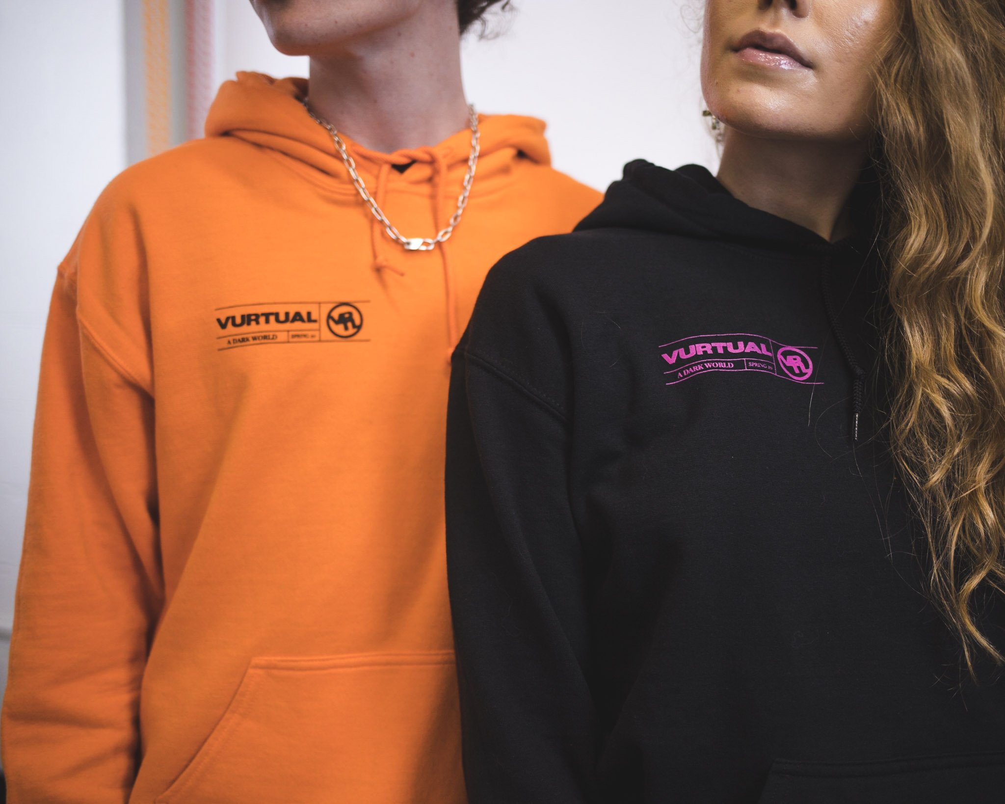 Close-up of two models wearing orange and black Vurtual hoodies with logo embroidery