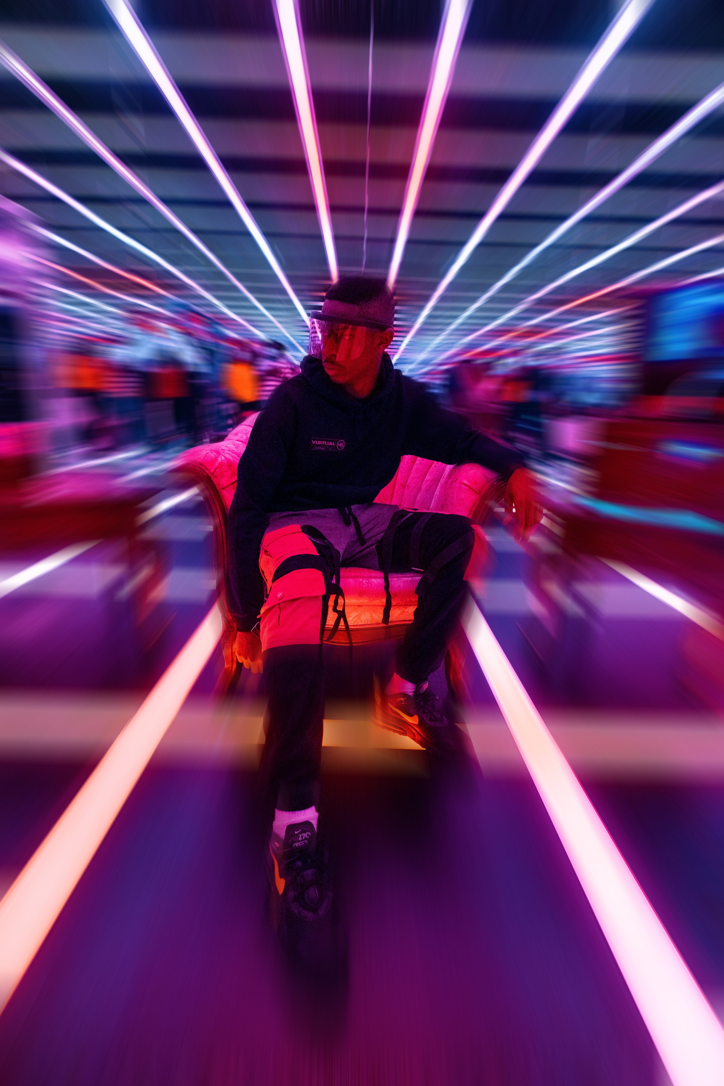 Man sitting on a chair in a neon light tunnel wearing Vurtual streetwear