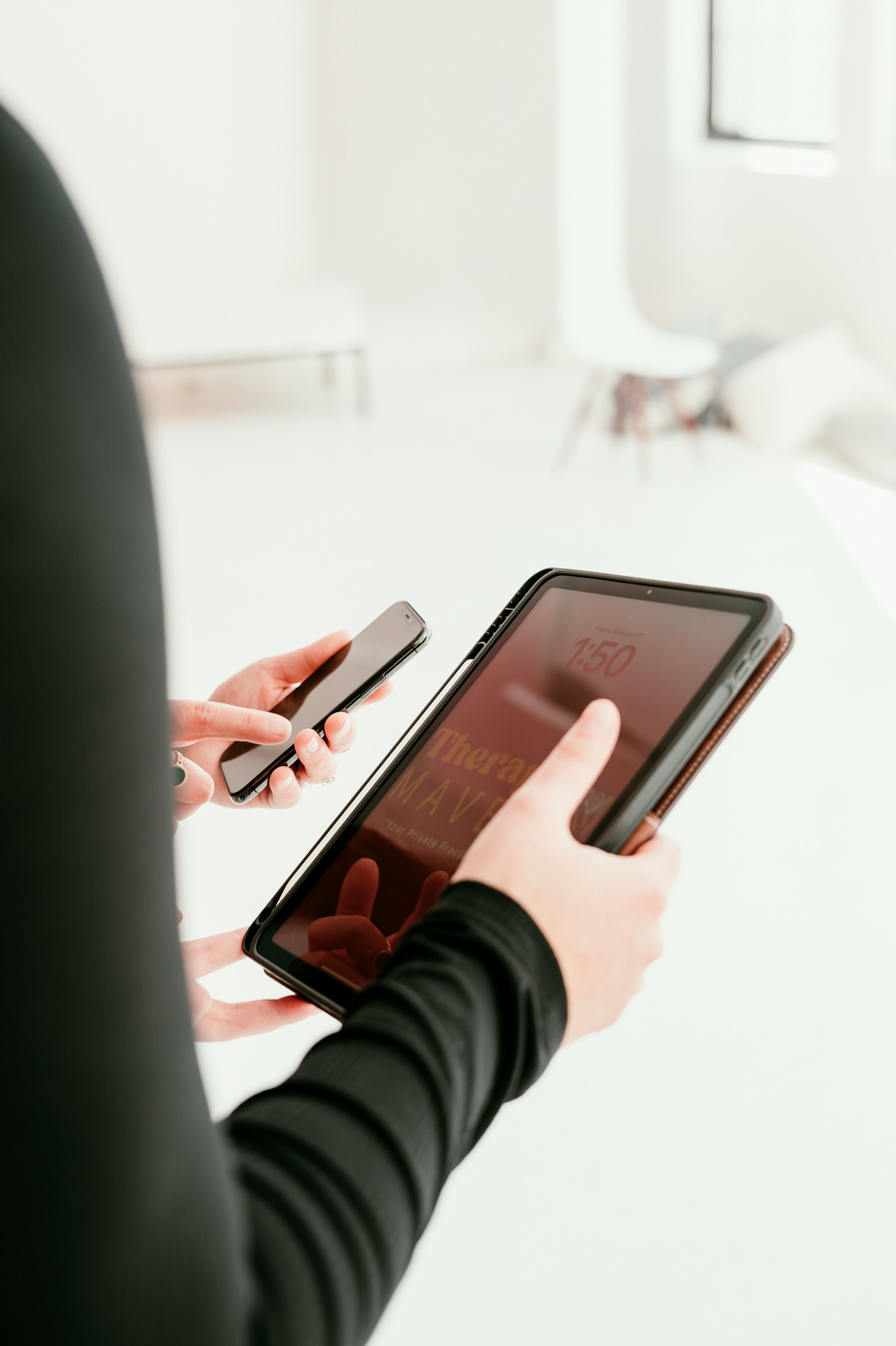 Person holding a large tablet and using a smartphone, in a well-lit room.