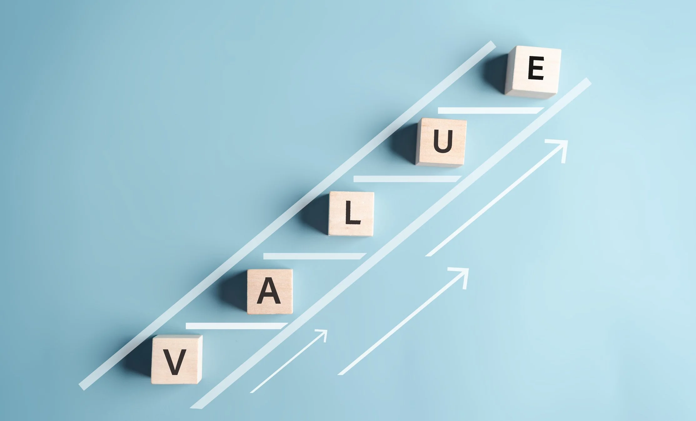 Wooden blocks spelling 'VALUE' arranged like a staircase against a light blue background, symbolizing uplifting and expanding how we value all people