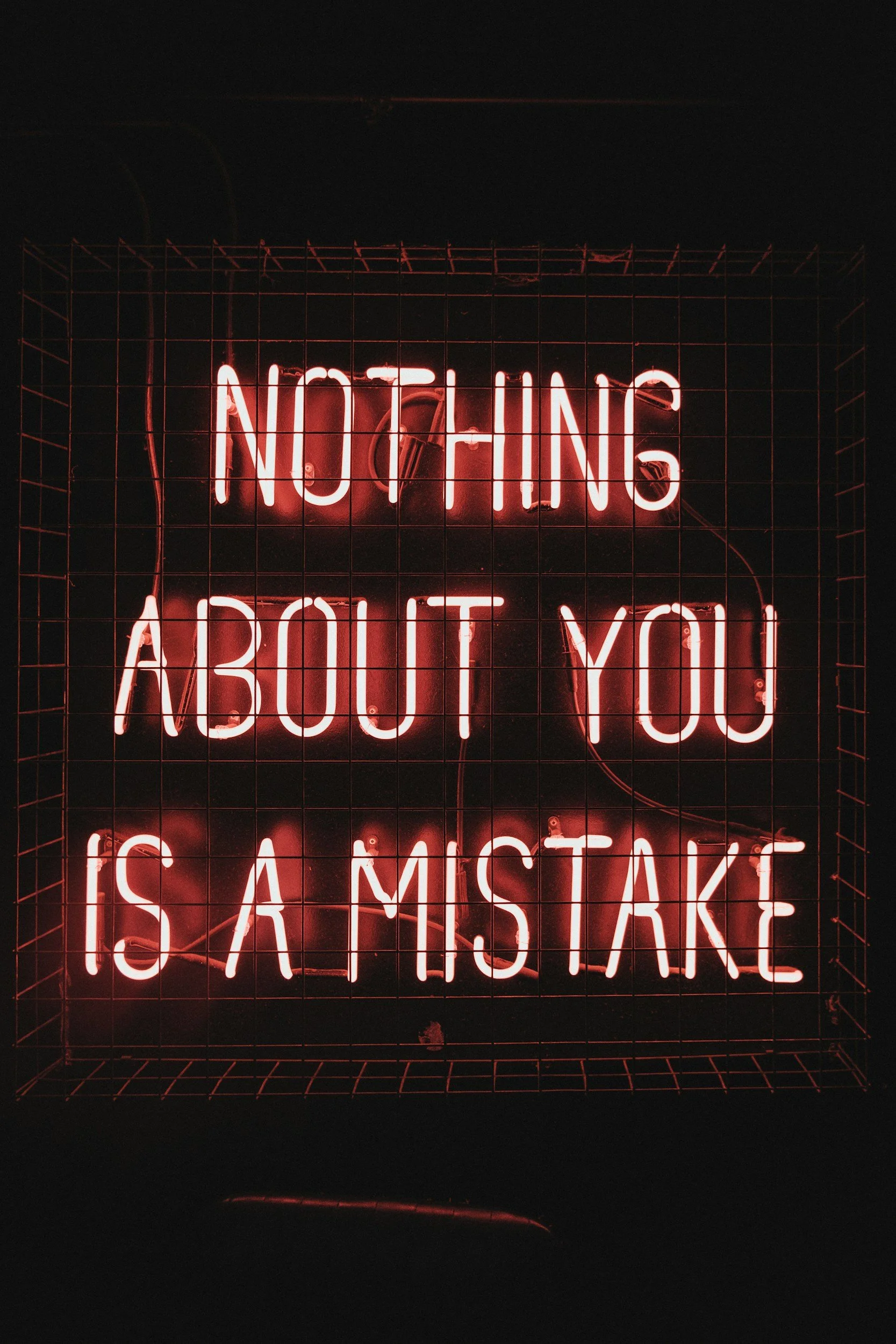 Neon sign reads 'Nothing About You Is A Mistake' in bright pink letters, enclosed in a wire grid.