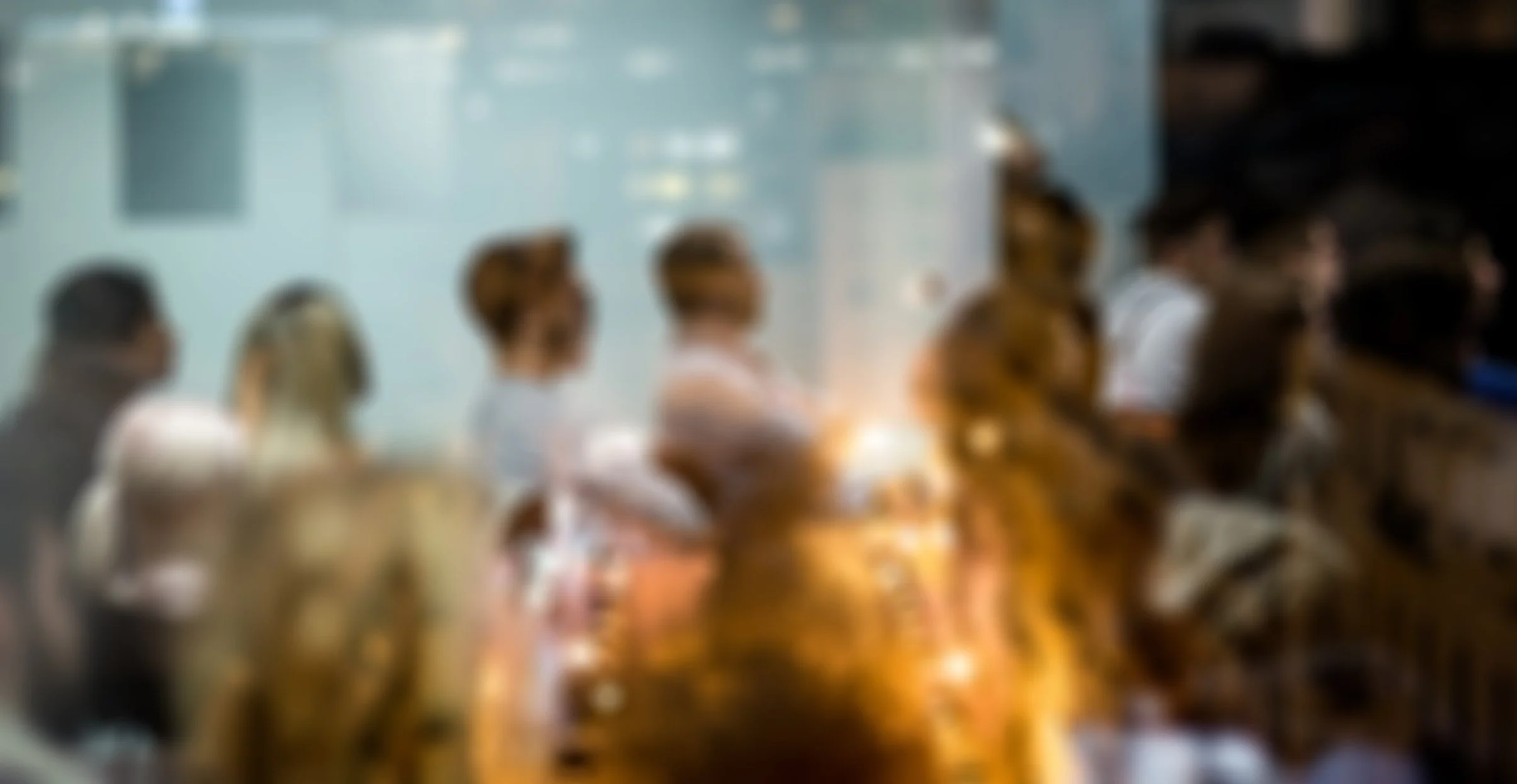 Blurred image of a group of people sitting at a long table indoors, possibly in a meeting or conference setting.