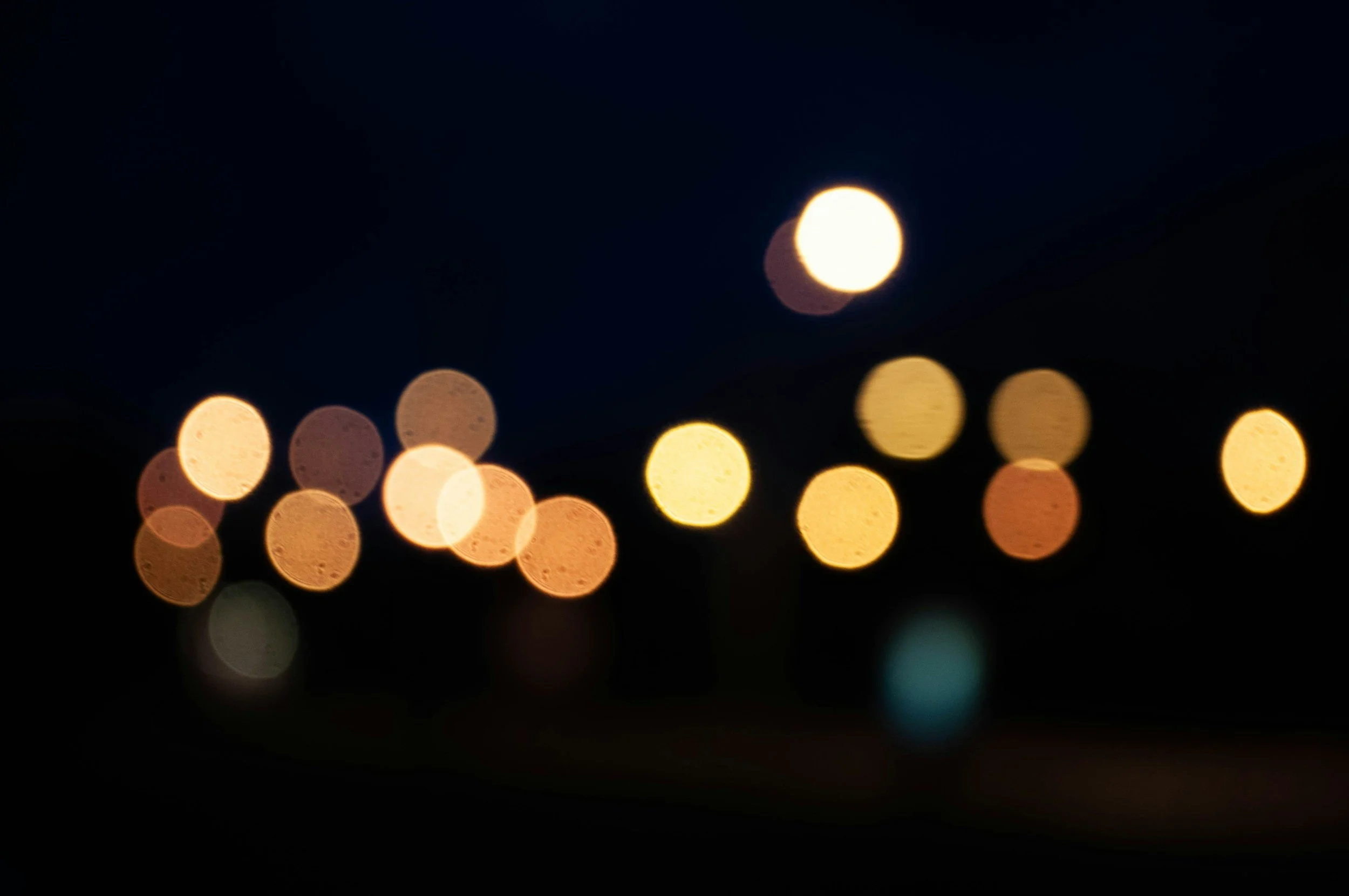Blurred city lights at night forming bokeh effects with a bright full moon or light source in the dark sky.