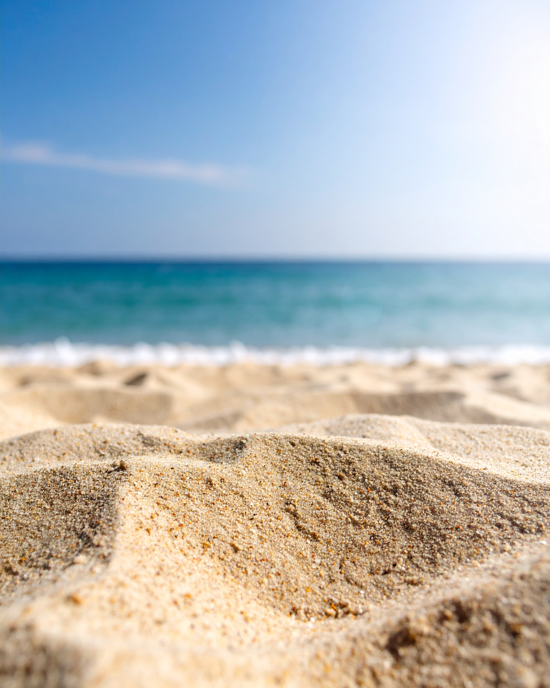 Close-up view of sandy beach with the ocean and blue sky in the background