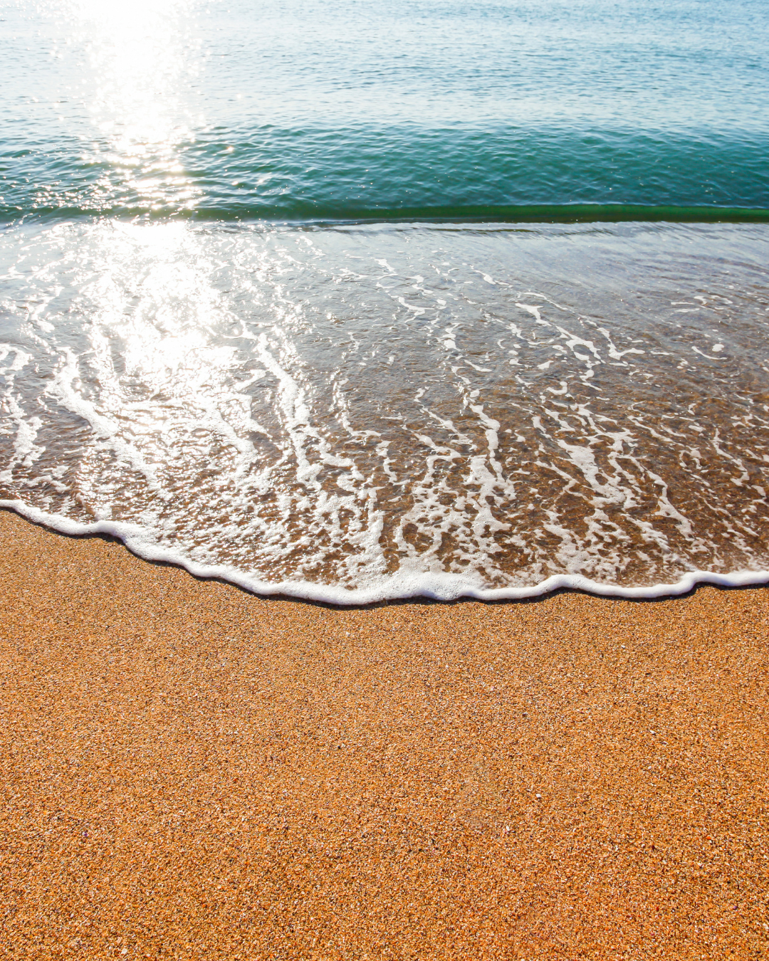 Sunlit ocean waves gently washing onto a sandy beach