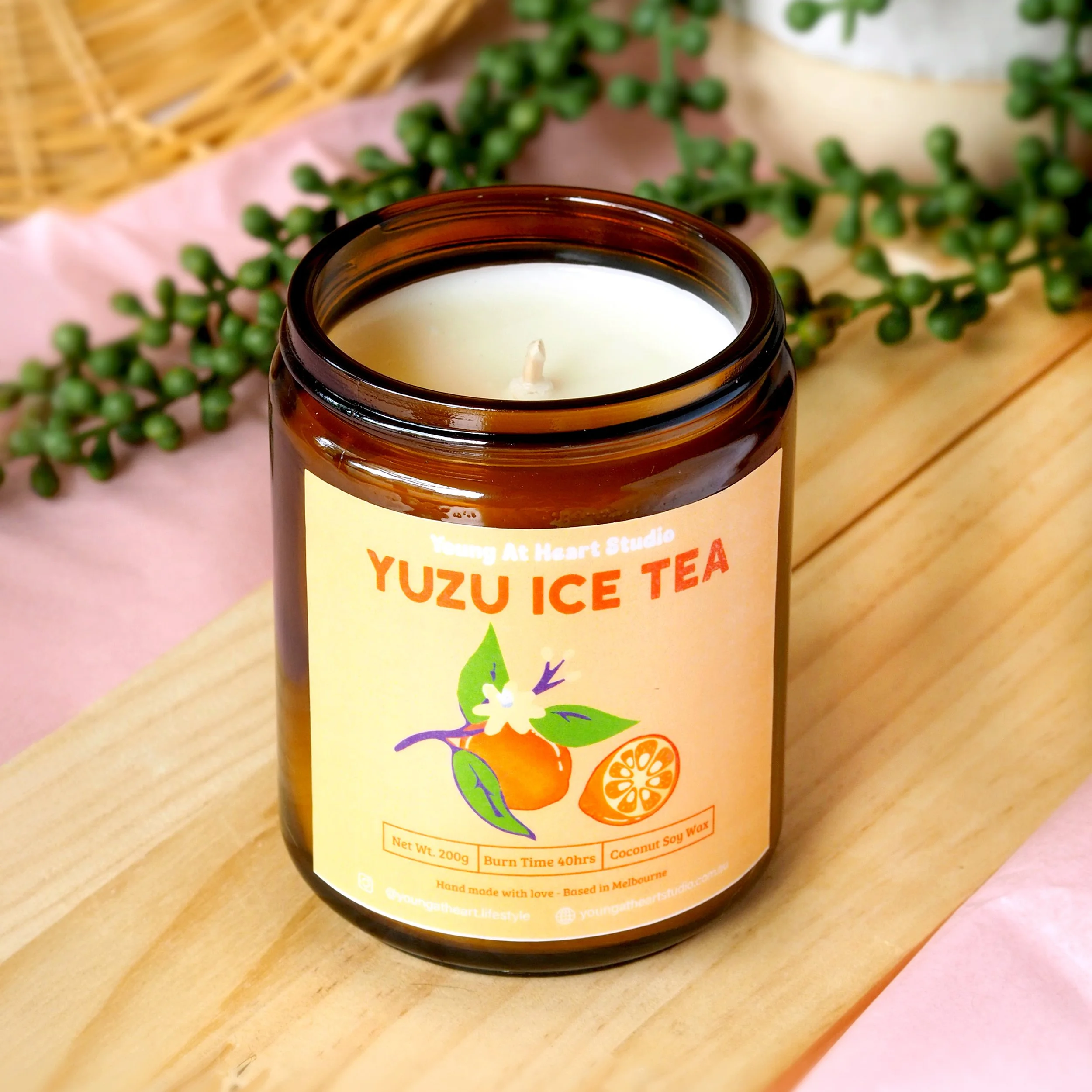 A lit candle in a glass jar labeled 'Yuzu Ice Tea,' placed on a small wooden stand.