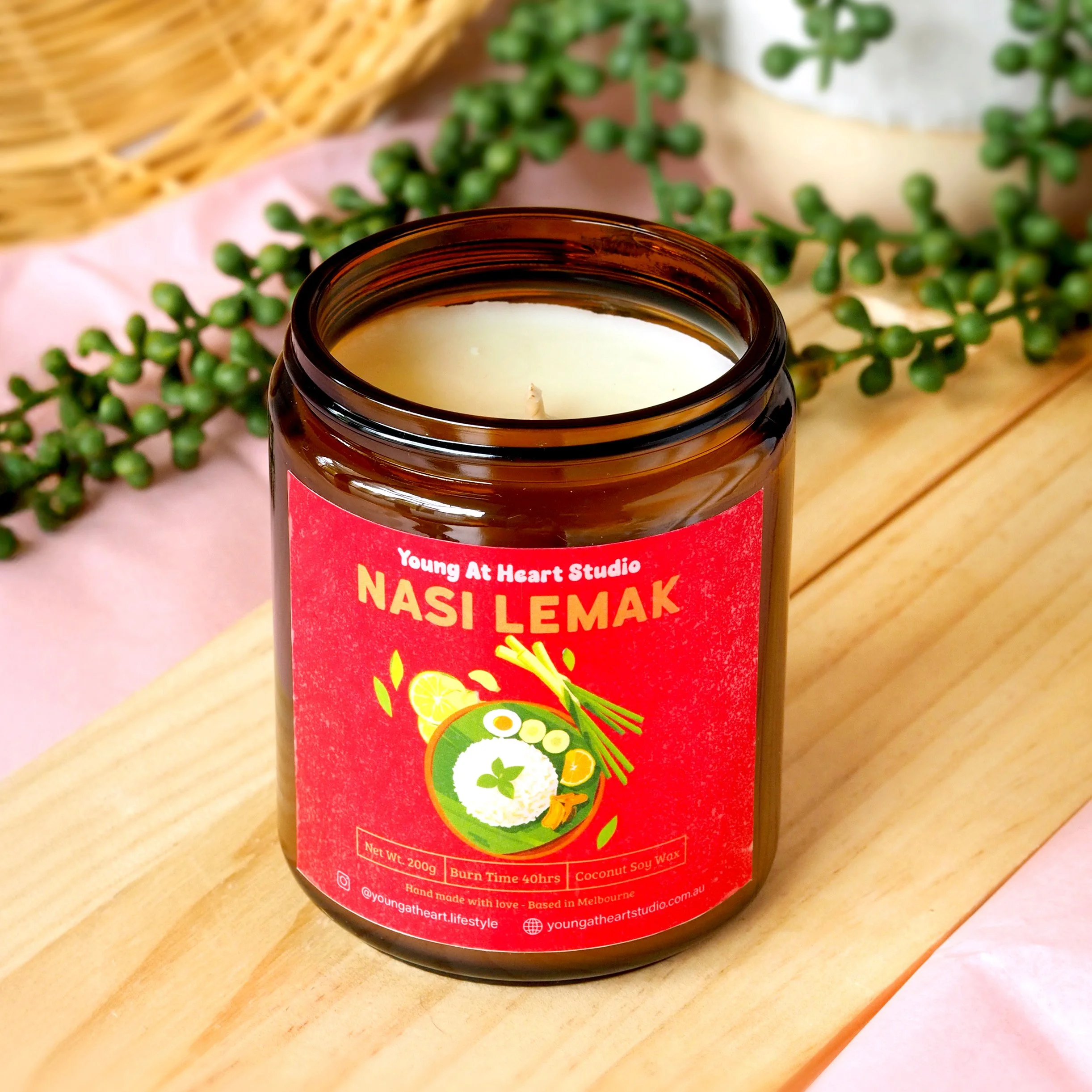 A clear glass jar with a red label containing a coconut-themed candle, placed on a light wooden block against a plain white background.