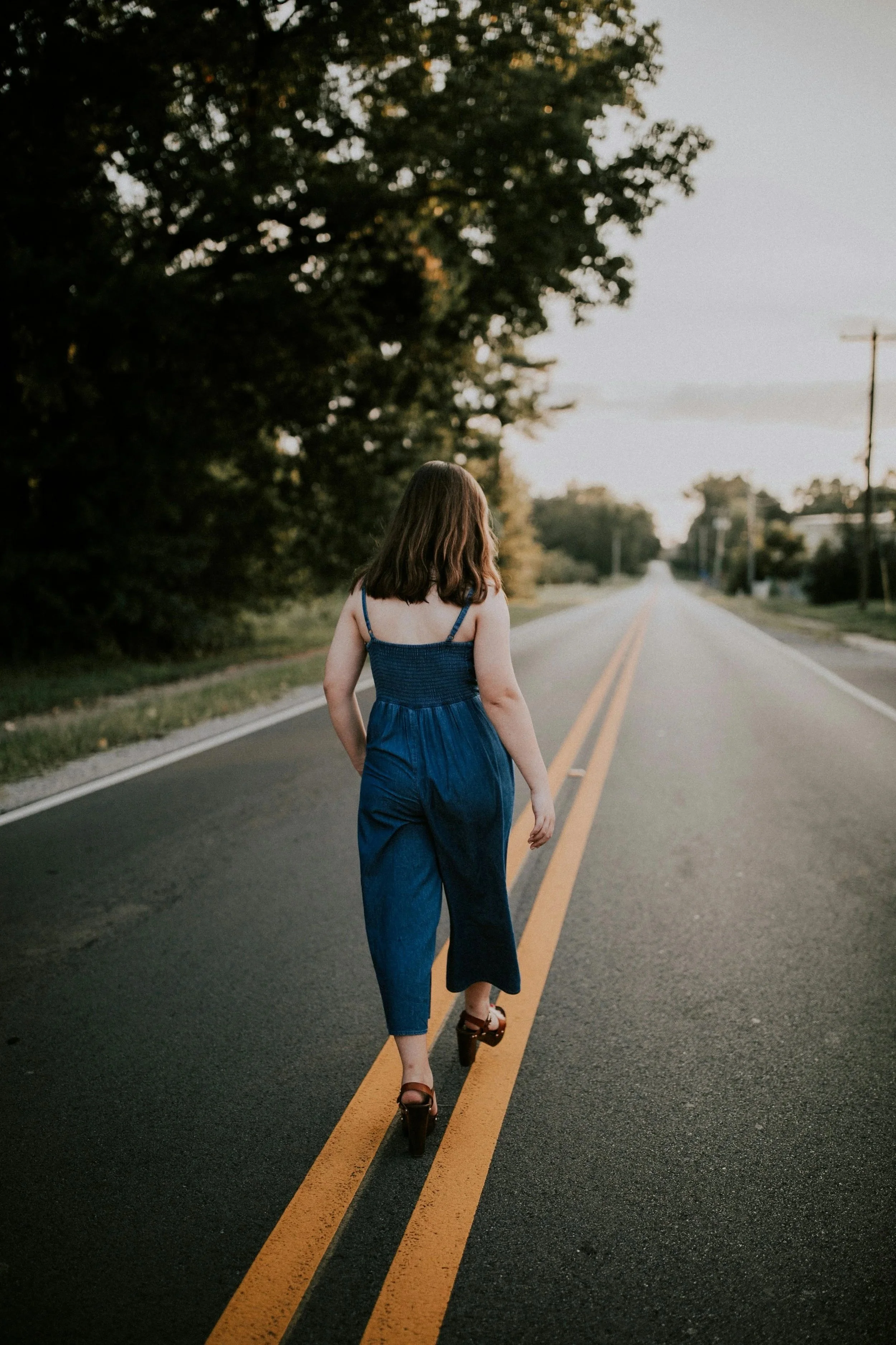 woman walking on yellow lines down paved road with purpose