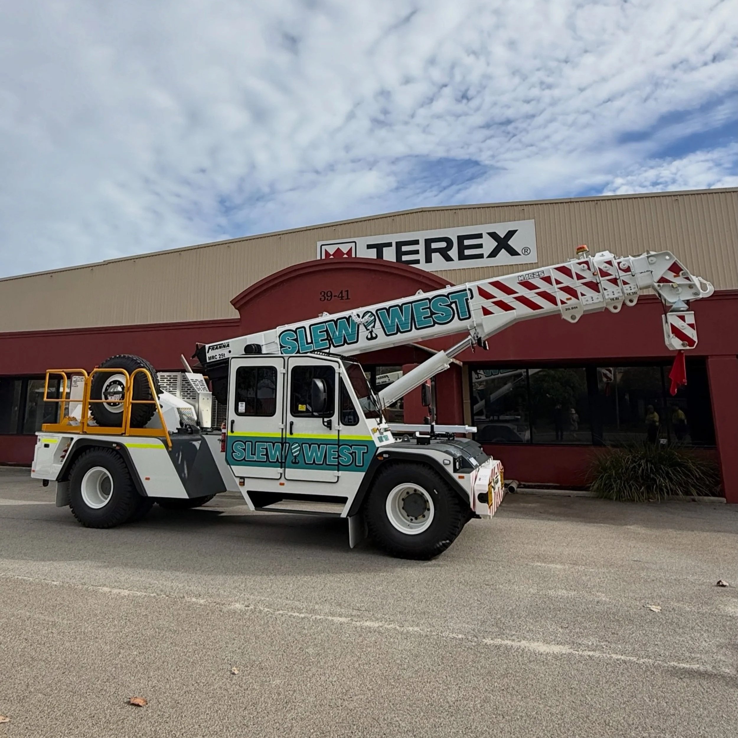 A construction vehicle, specifically a bucket truck, parked in front of a building with the sign TEREX. The sky is partly cloudy.