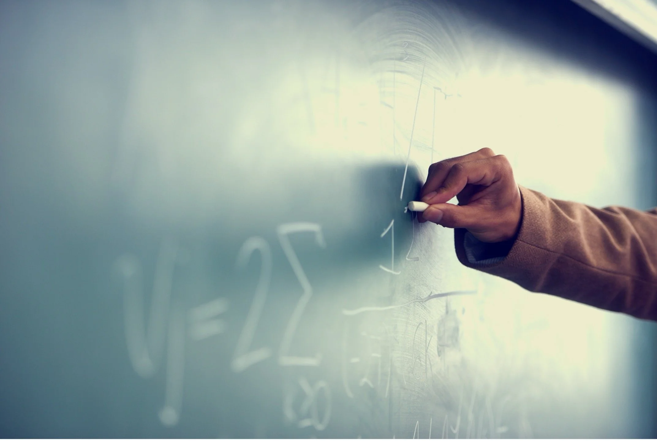 A person writing mathematical equations on a blackboard with white chalk.